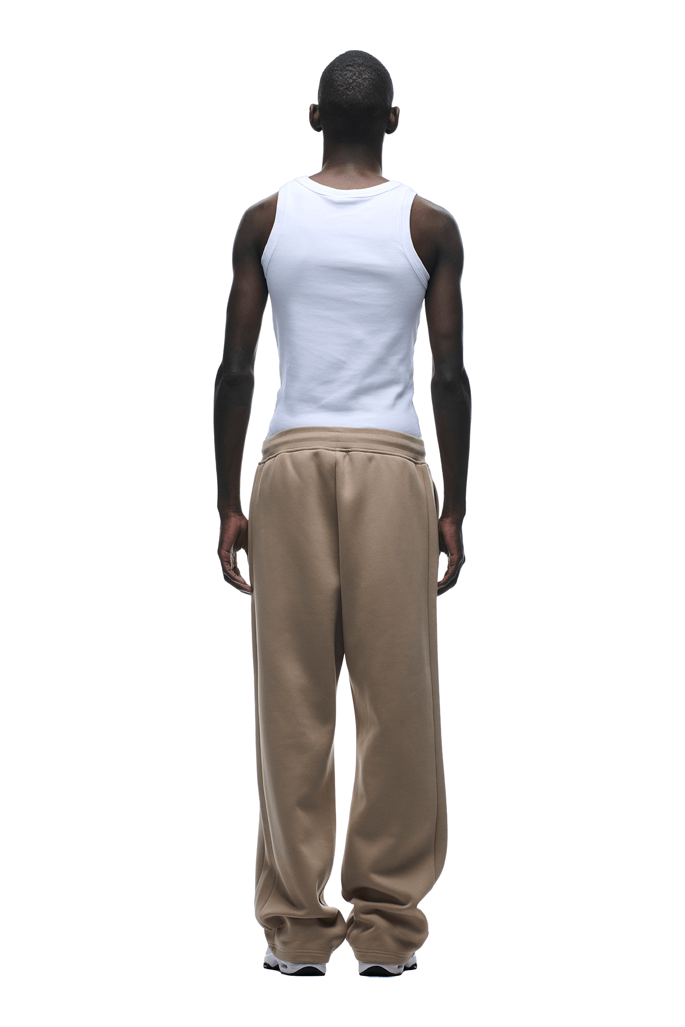 A person stands facing away, wearing a white tank top and 6PMs OPEN LEG JOGGER MOCCA CREAM sweatpants with a stacking length, arms relaxed by their sides against a transparent background.