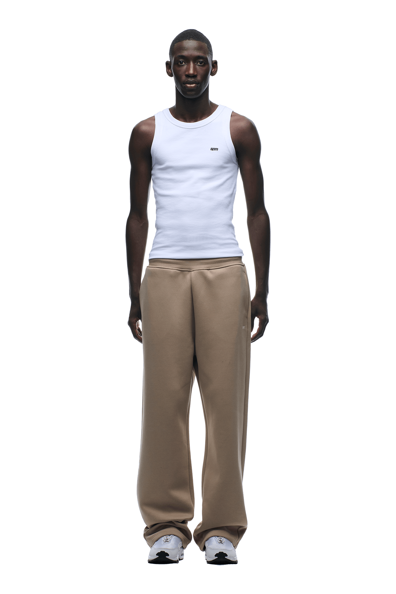 A man faces forward in a modern classic style, wearing a white sleeveless tank top, 6PM OPEN LEG JOGGER MOCCA CREAM pants, and white sneakers against a plain background.