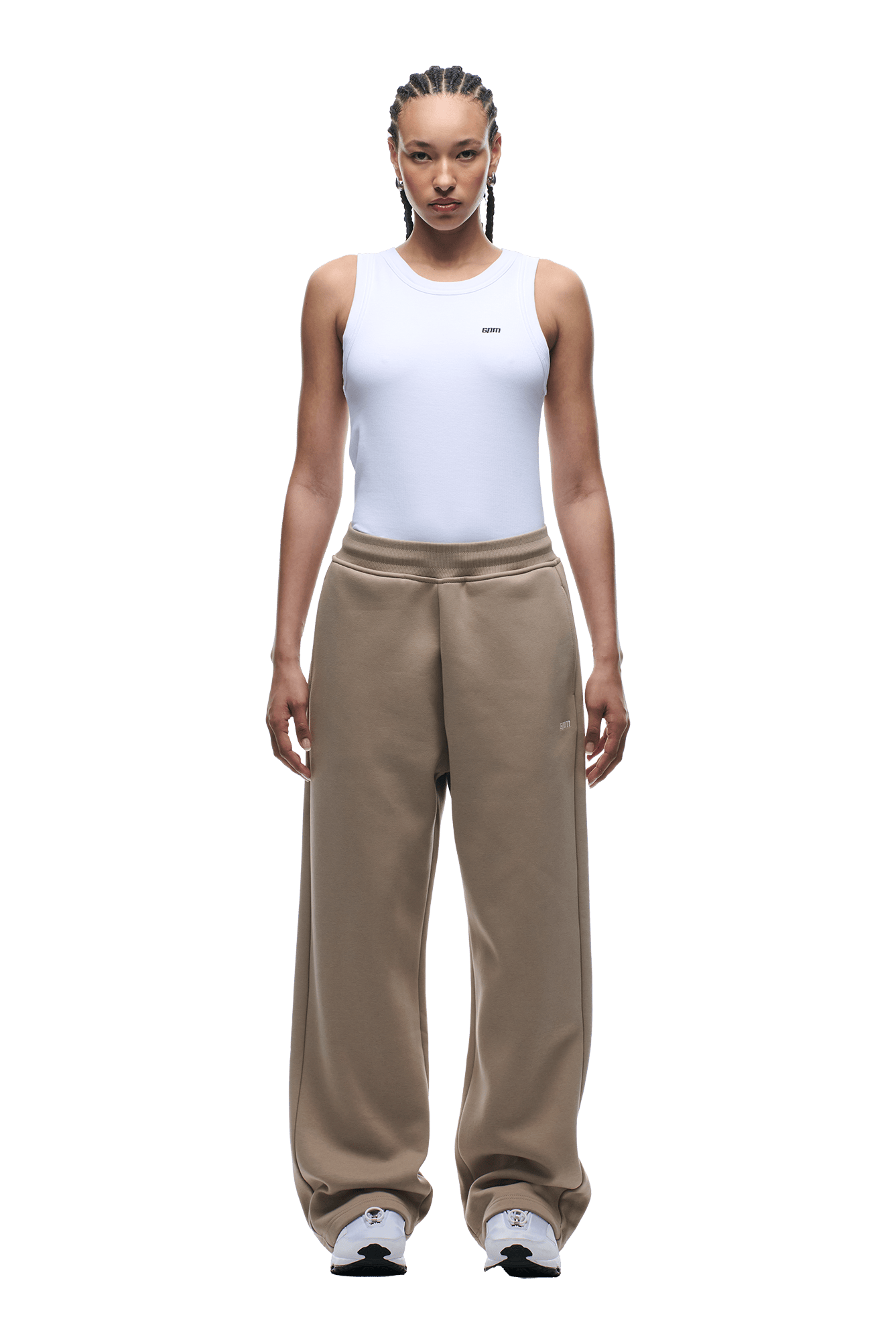 A person with braided hair and a neutral expression wears a white sleeveless top, 6PM OPEN LEG JOGGER MOCCA CREAM sweatpants, and white sneakers. The background is transparent, highlighting a modern classic look.
