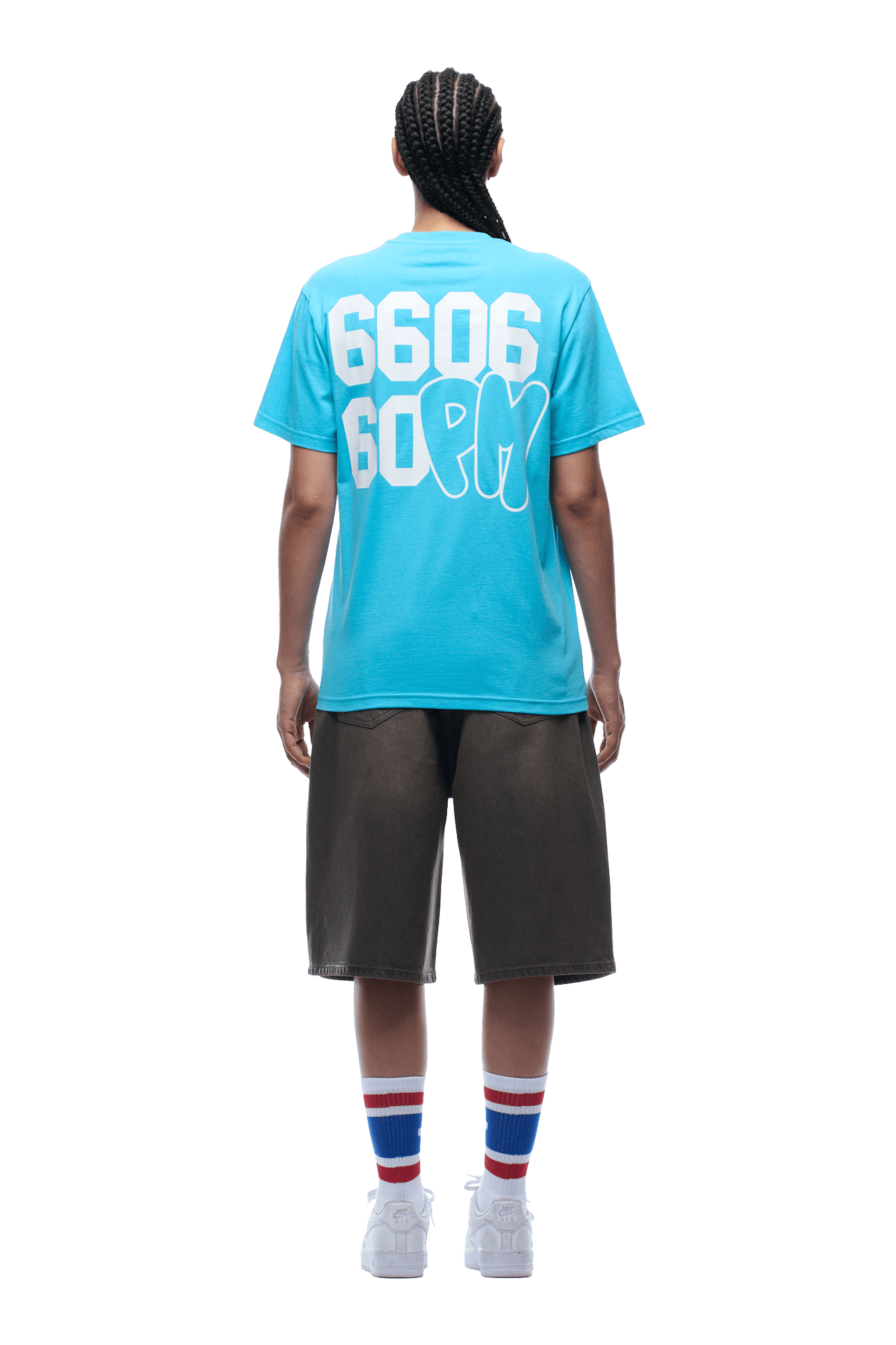 A person with braided hair stands facing away, wearing the 6PM 660660 TEE BLUE featuring large white print, paired with black knee-length shorts, white sneakers, and white socks accented by red and blue stripes.