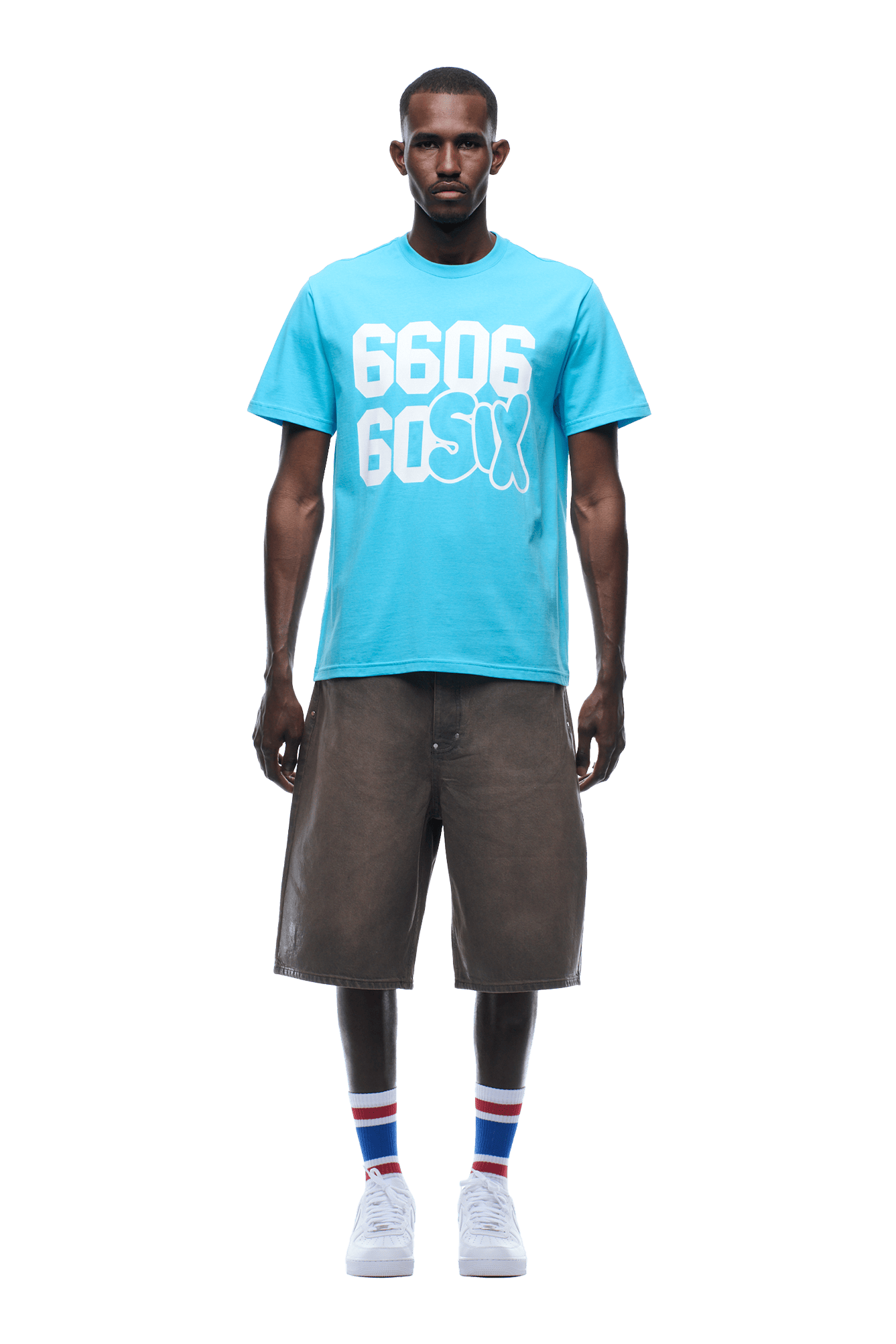 A man faces forward wearing a 6PM 660660 TEE BLUE, paired with loose brown knee-length shorts, white sneakers, and white socks featuring red and blue stripes.