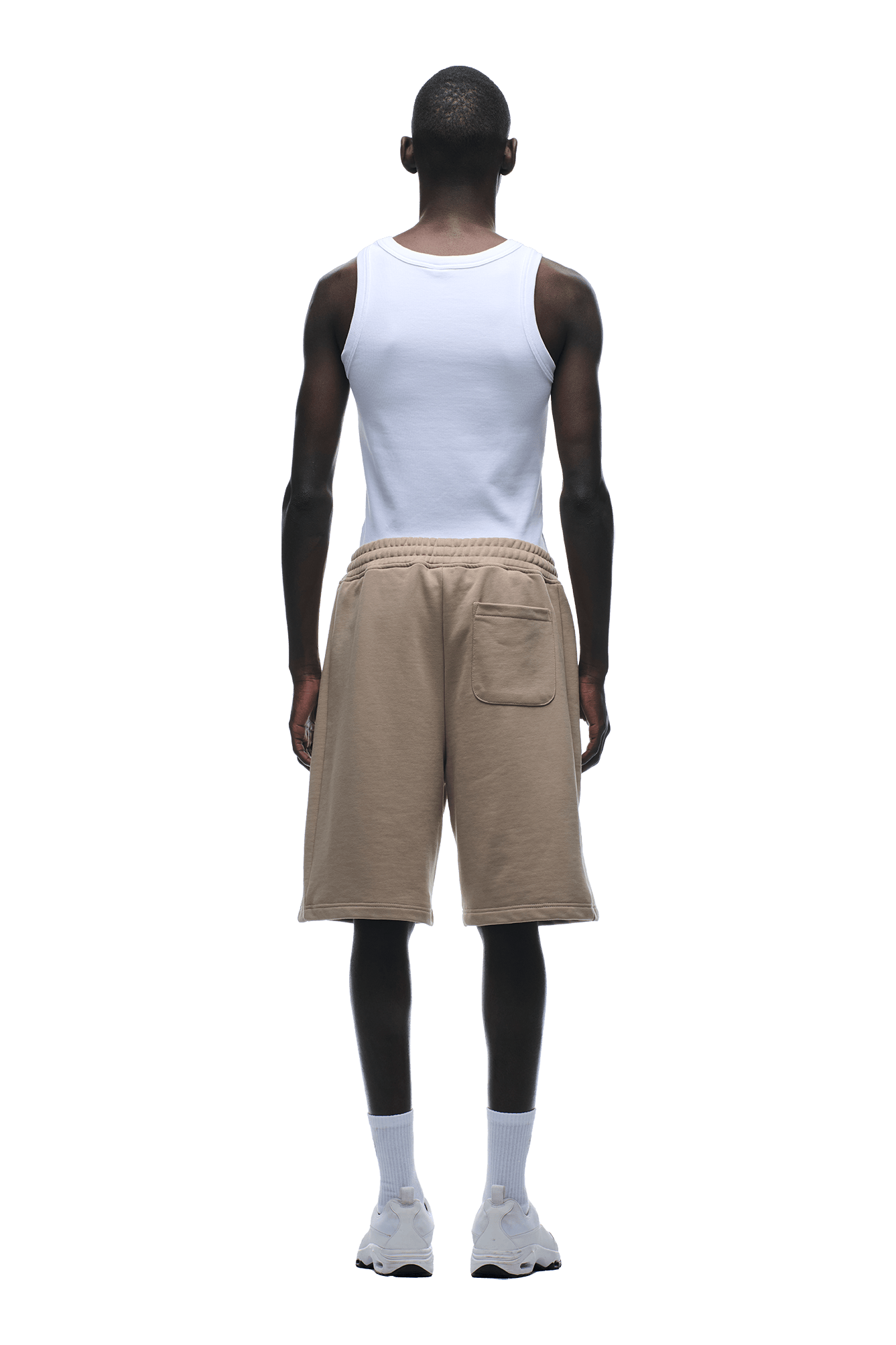 A man faces away, wearing a white tank top and 6PM 6PM+ SHORTS MOCCA CREAM—relaxed fit, beige knee-length shorts with a back pocket—paired with white crew socks and sneakers against a plain background.