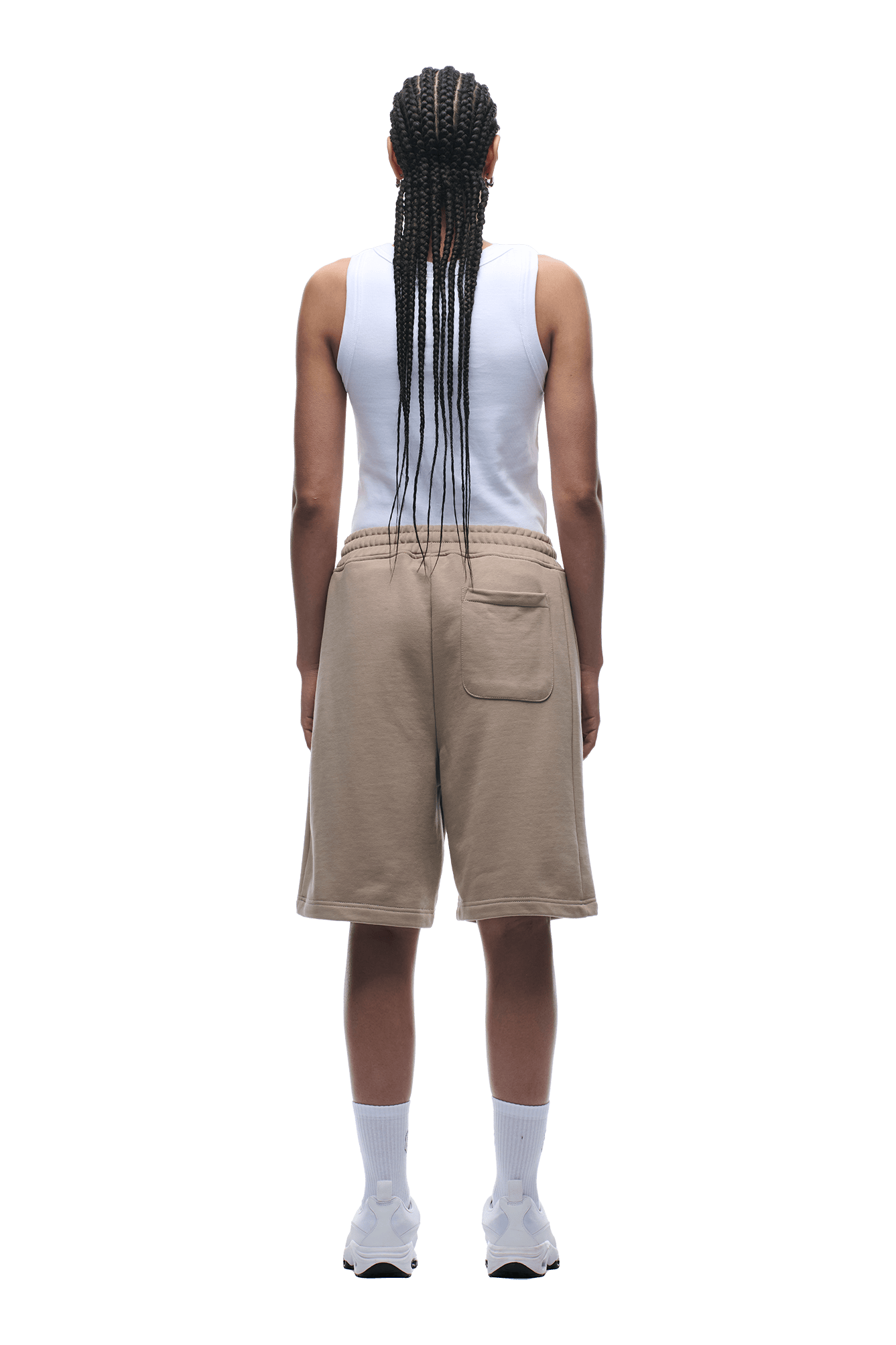 A person with long braids, wearing a white tank top and 6PM 6PM+ SHORTS MOCCA CREAM featuring a drawstring waist for a relaxed fit, along with white socks and sneakers, stands facing away from the camera against a plain background.