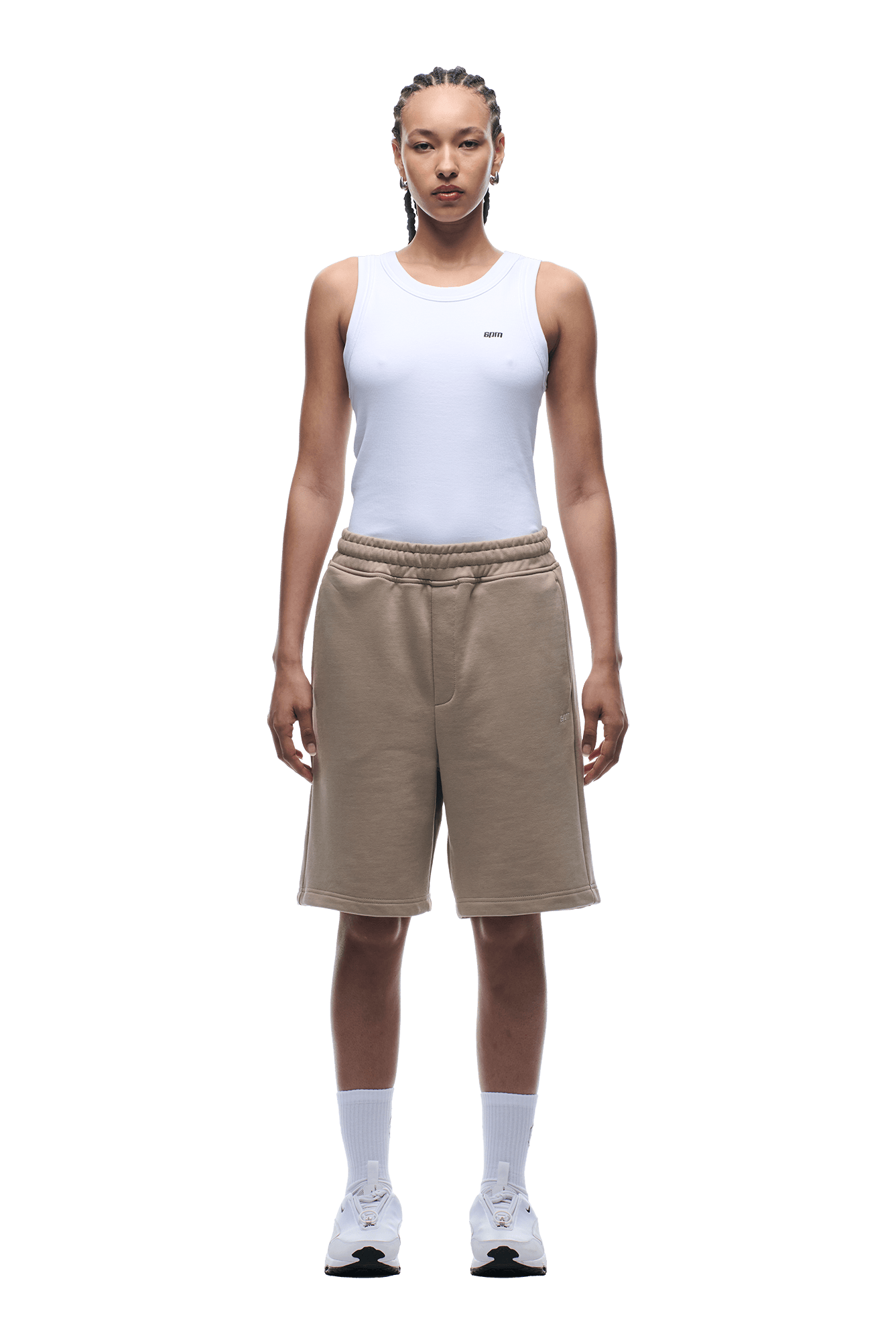A person stands facing forward in a white sleeveless tank top and 6PM+ SHORTS MOCCA CREAM by 6PM with a relaxed fit, paired with white crew socks and sneakers, perfect for lounging against a plain background.