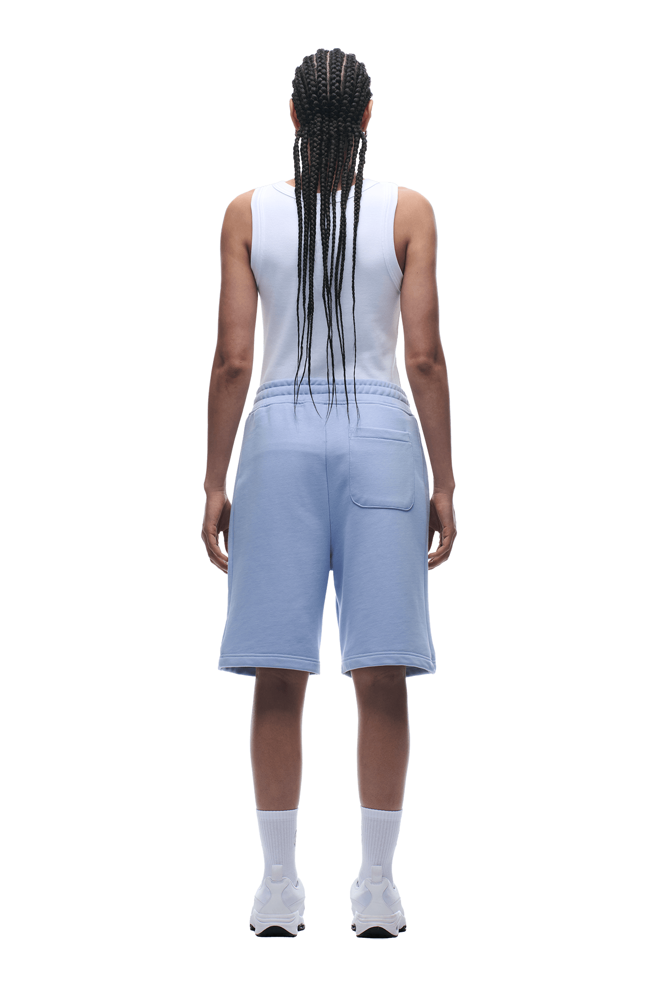 A person with long braided hair faces away, wearing a white tank top and 6PM+ SHORTS SOFT VIOLET—light blue, knee-length shorts with a drawstring waist—plus white socks and sneakers, on a transparent background.