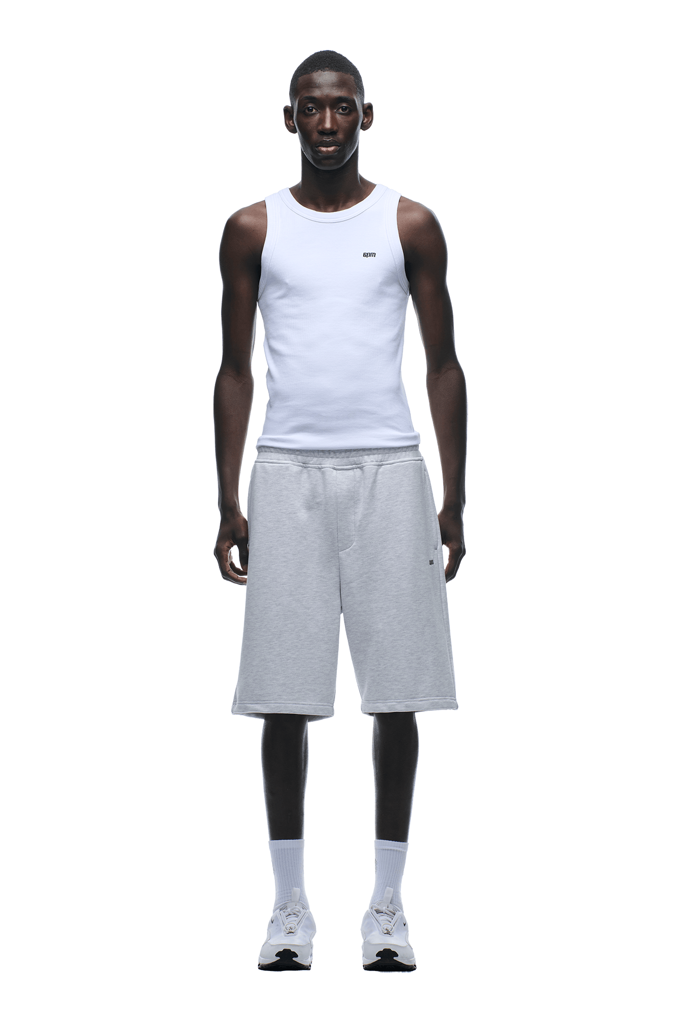 A man faces forward wearing a relaxed fit white tank top and 6PM 6PM+ SHORTS LIGHT GREY, paired with white socks and sneakers, set against a plain background.