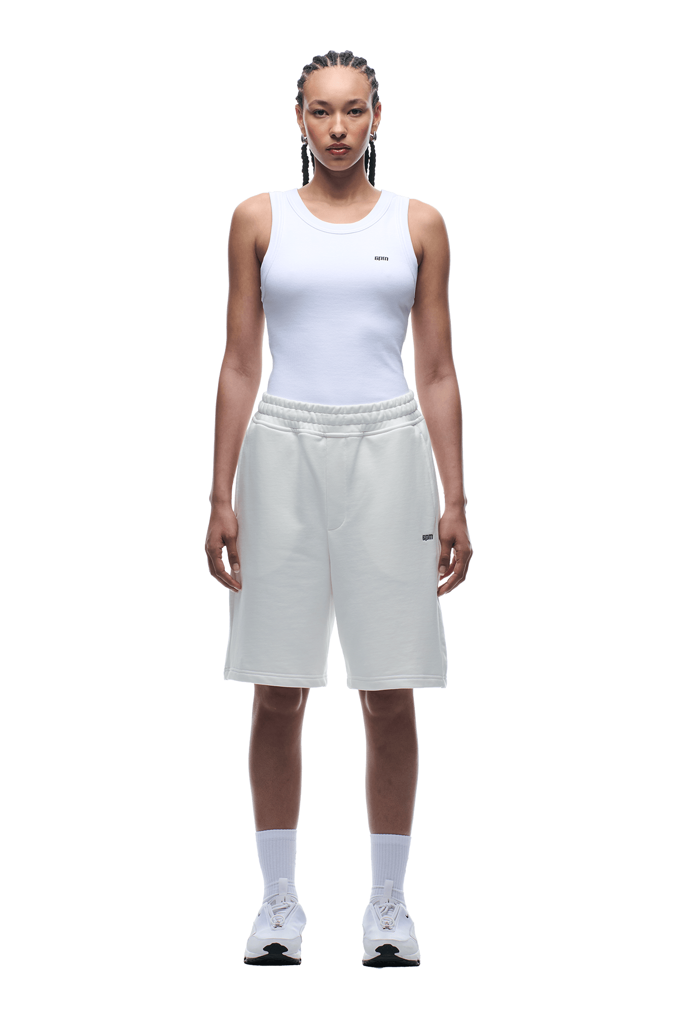 A person stands facing forward in a white tank top and 6PM 6PM+ SHORTS COCONUT WHITE, featuring a relaxed fit and drawstring waist, paired with white socks and sneakers. Their hair is in braids, and the background is transparent.