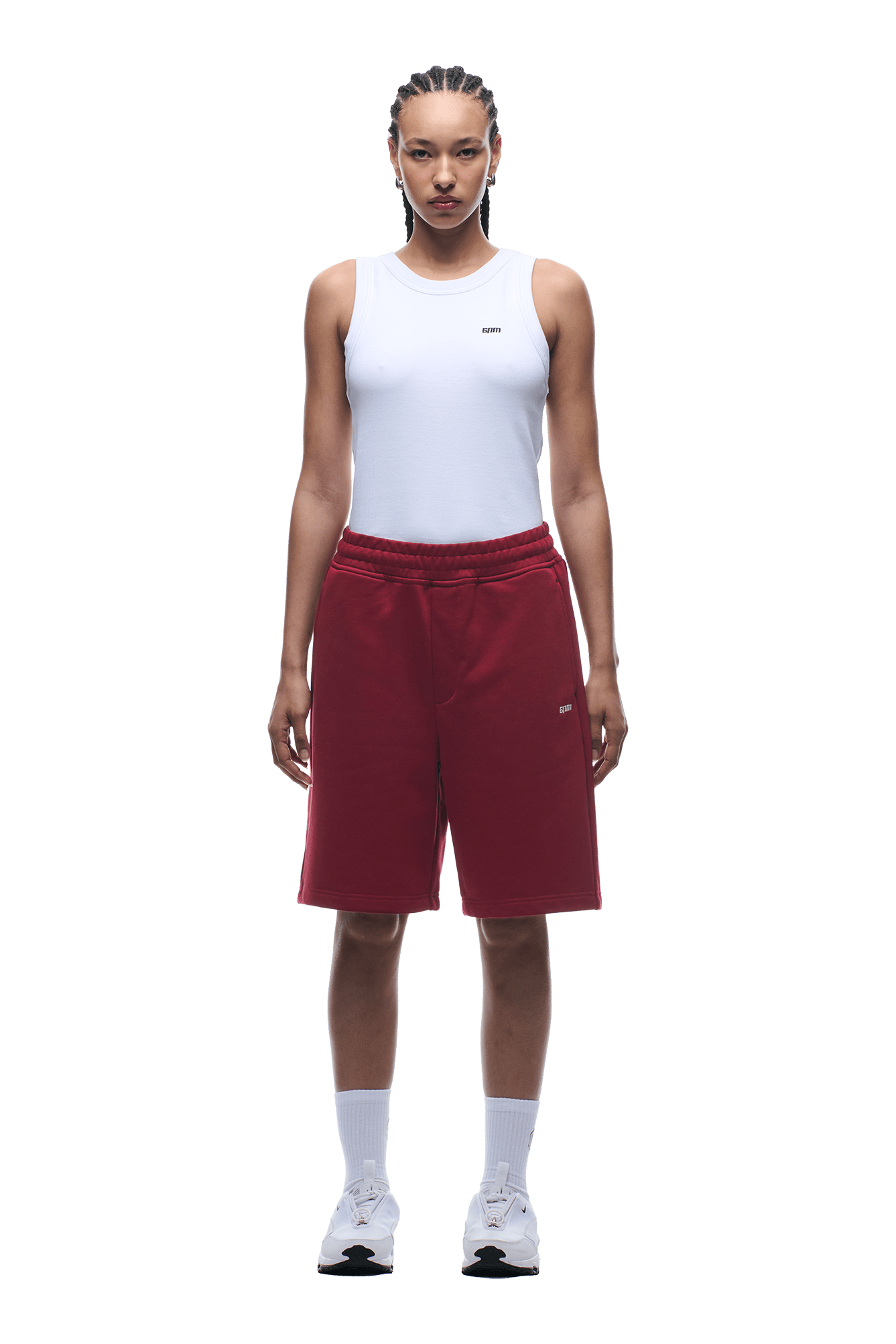 A person stands facing forward, wearing a white sleeveless top and 6PM+ SHORTS WINE RED by 6PM, paired with white socks and sneakers. The background is transparent.