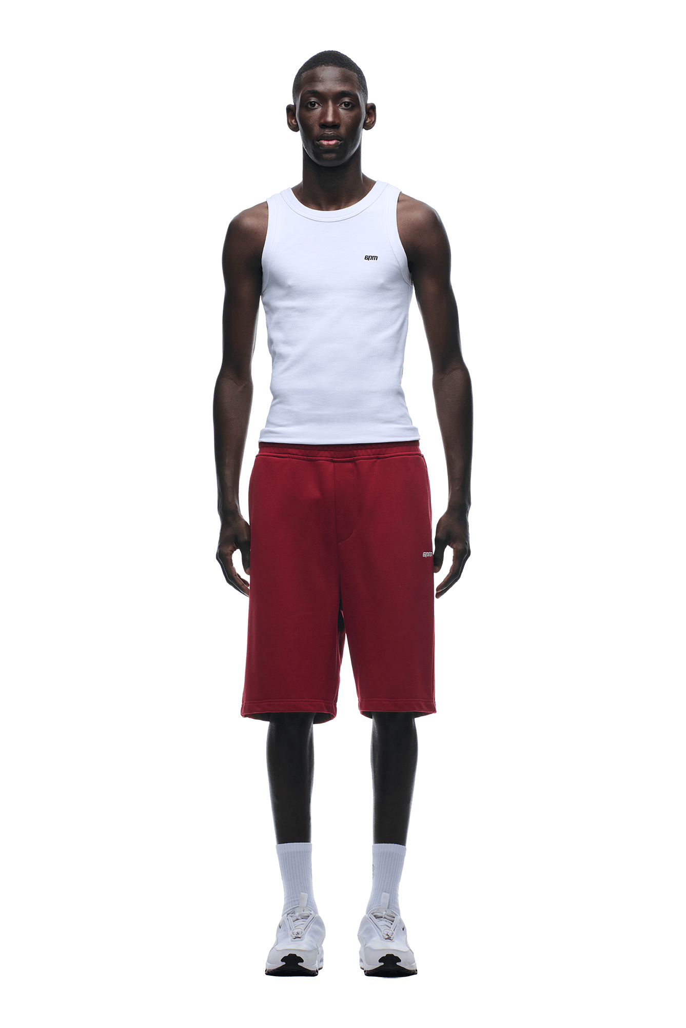 A man faces forward in a white sleeveless tank top and 6PM 6PM+ SHORTS WINE RED, featuring a relaxed fit and drawstring waist, paired with white socks and sneakers, against a plain green background.