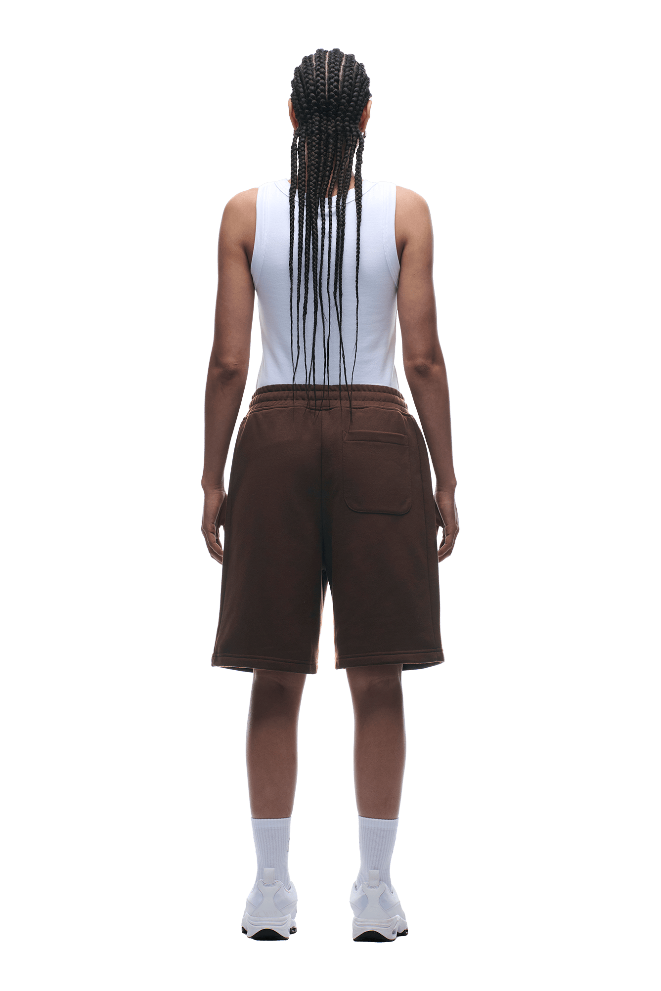Person with long braids wears a white sleeveless top and 6PM+ SHORTS CHOCOLATE BROWN by 6PM—relaxed fit, knee-length with drawstring waist—plus white socks and sneakers, facing away from the camera on a transparent background.