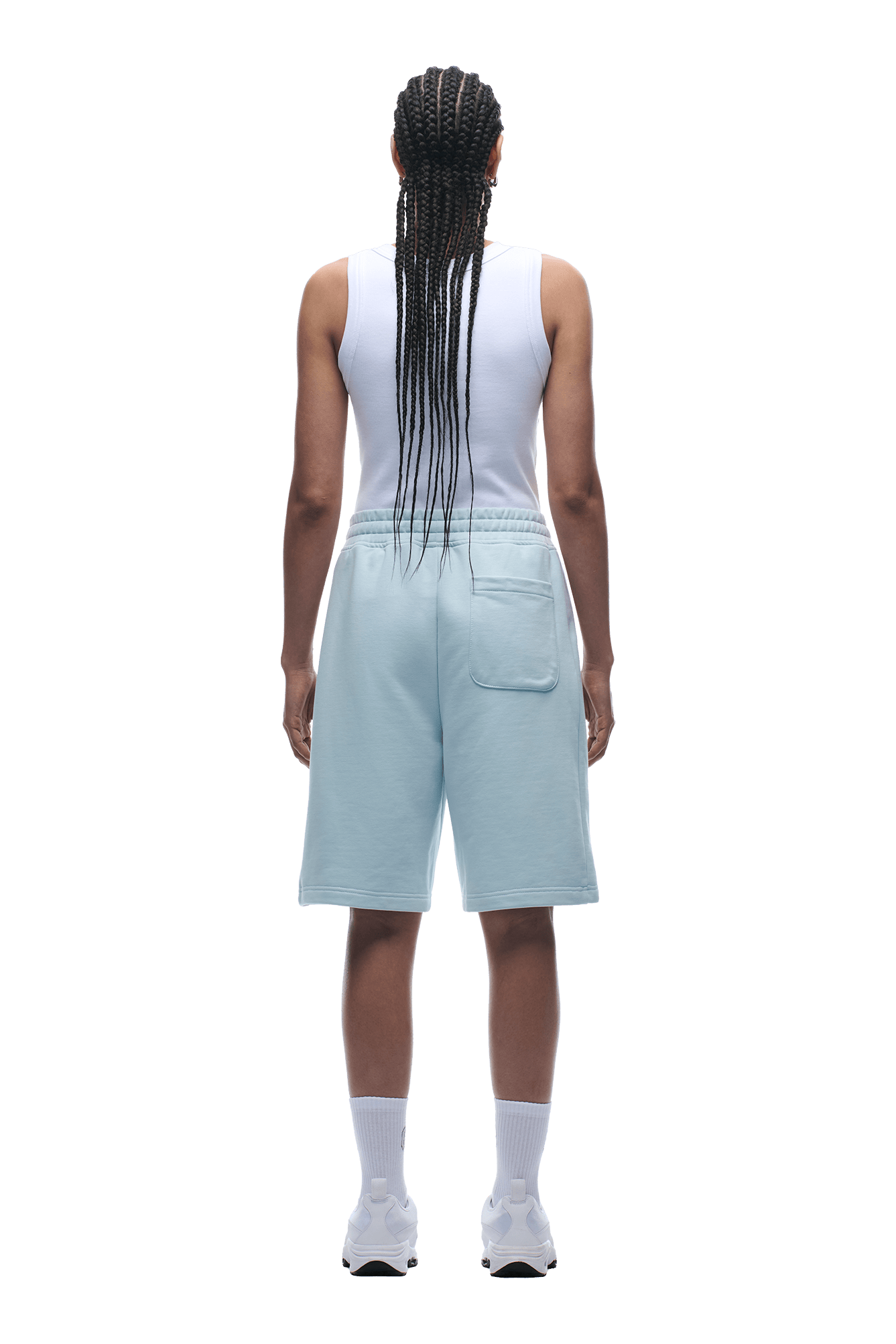 A person with long braids, wearing a white tank top and 6PM+ SHORTS ICE BLUE with a relaxed fit, plus white socks and sneakers, stands facing away from the camera against a plain background.
