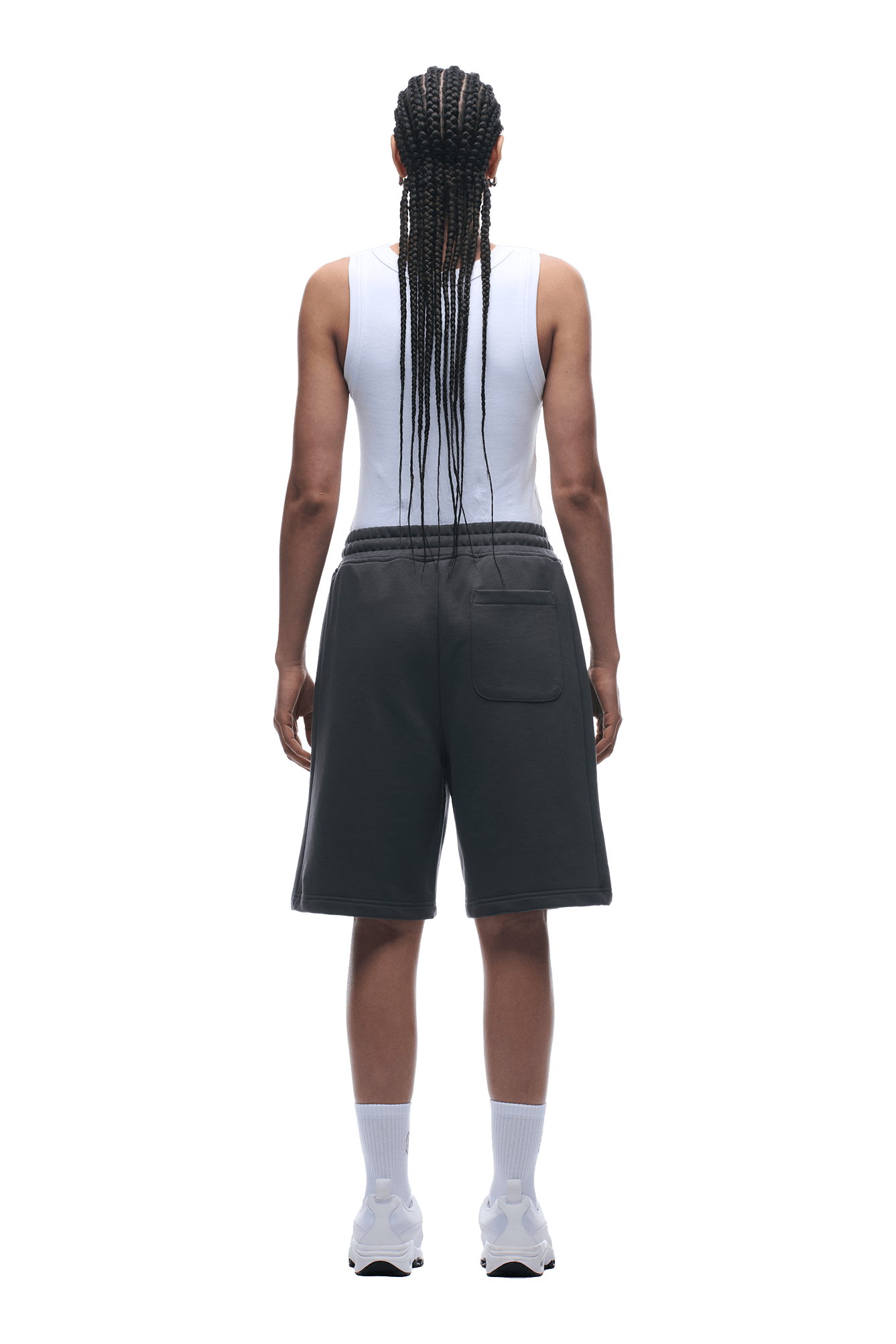 A person with long braids stands with their back to the camera, wearing a white tank and 6PM 6PM+ SHORTS ANTHRACITE, paired with white socks and sneakers against a plain background.