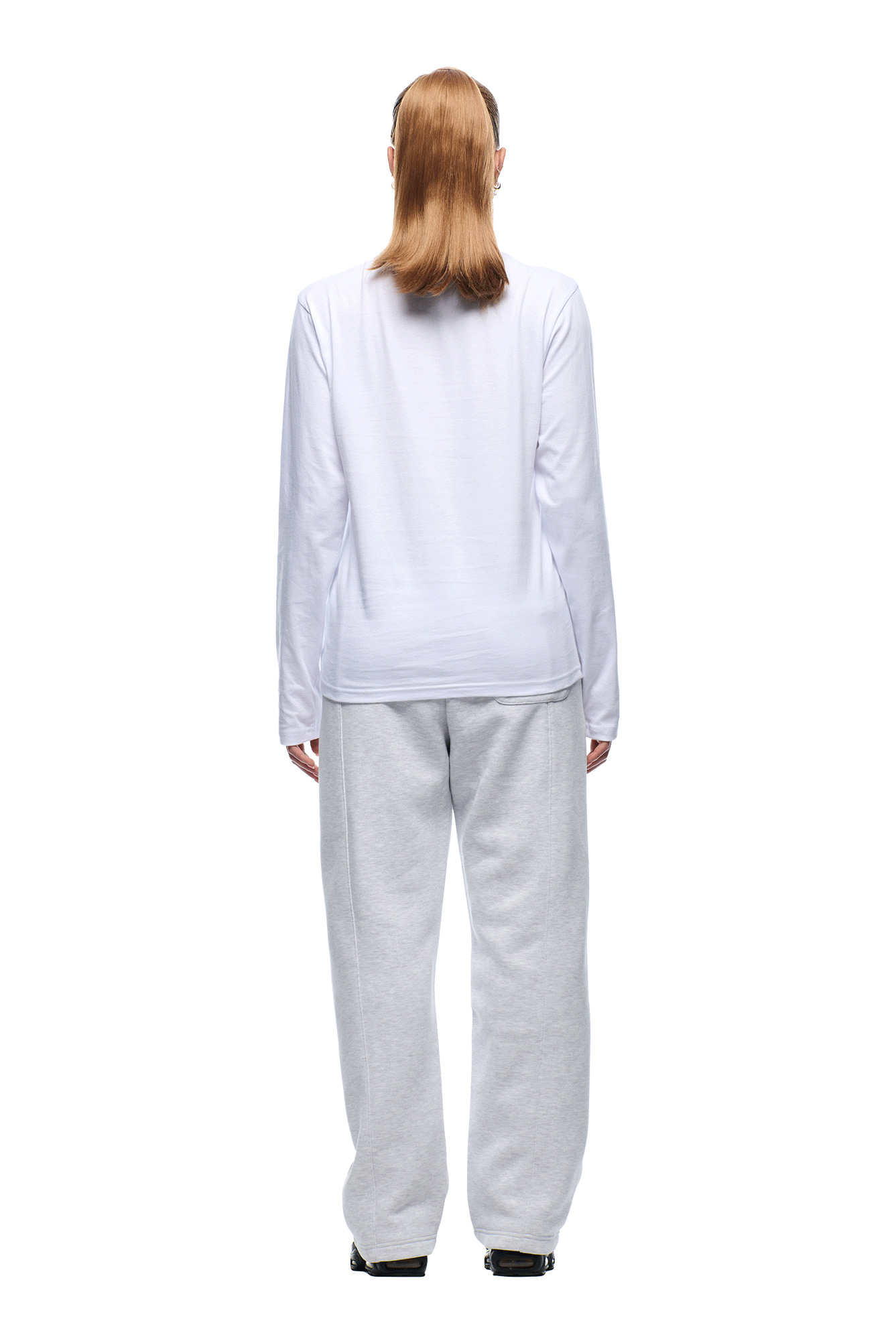 A person with straight, shoulder-length light brown hair faces away in a 6PM 6PM+ SLIM FIT LONGSLEEVE WHITE and light gray sweatpants, standing against a plain white background for a minimalist look.