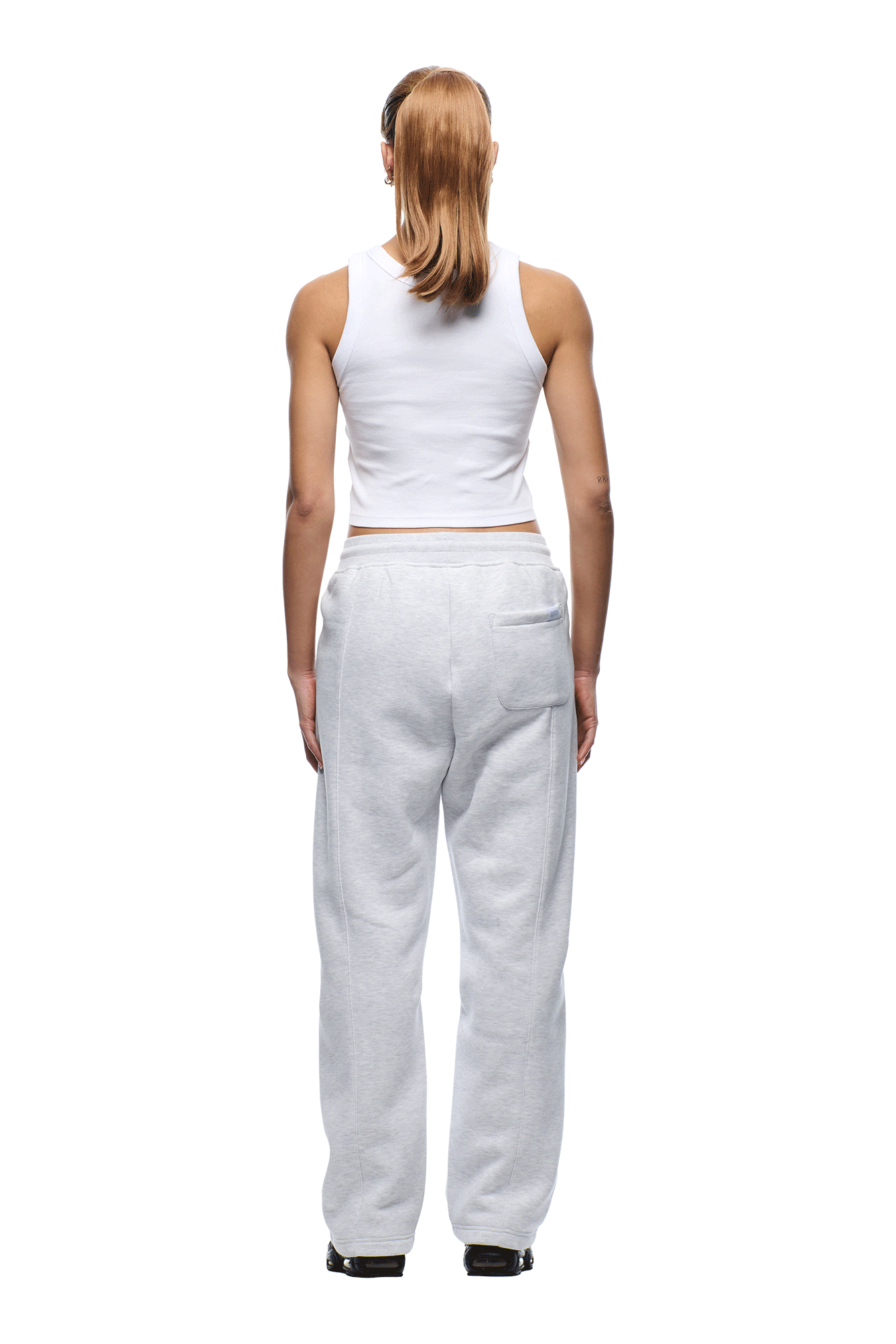 A person with long, light brown hair in a ponytail is standing facing away, wearing a white sleeveless crop top and 6PM 6PM+ Slim Fit Jogger Light Grey sweatpants with black shoes against a white background.