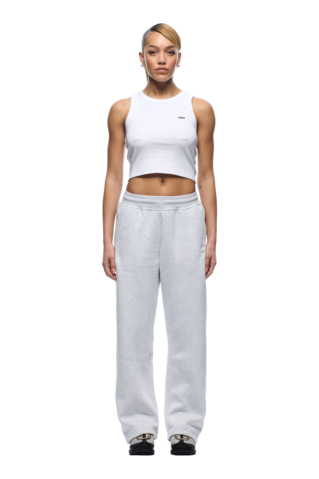 A person stands facing forward against a plain white background, wearing the 6PM+ SLIM FIT JOGGER LIGHT GREY by 6PM, paired with a white sleeveless crop top and black sneakers with gold accents.