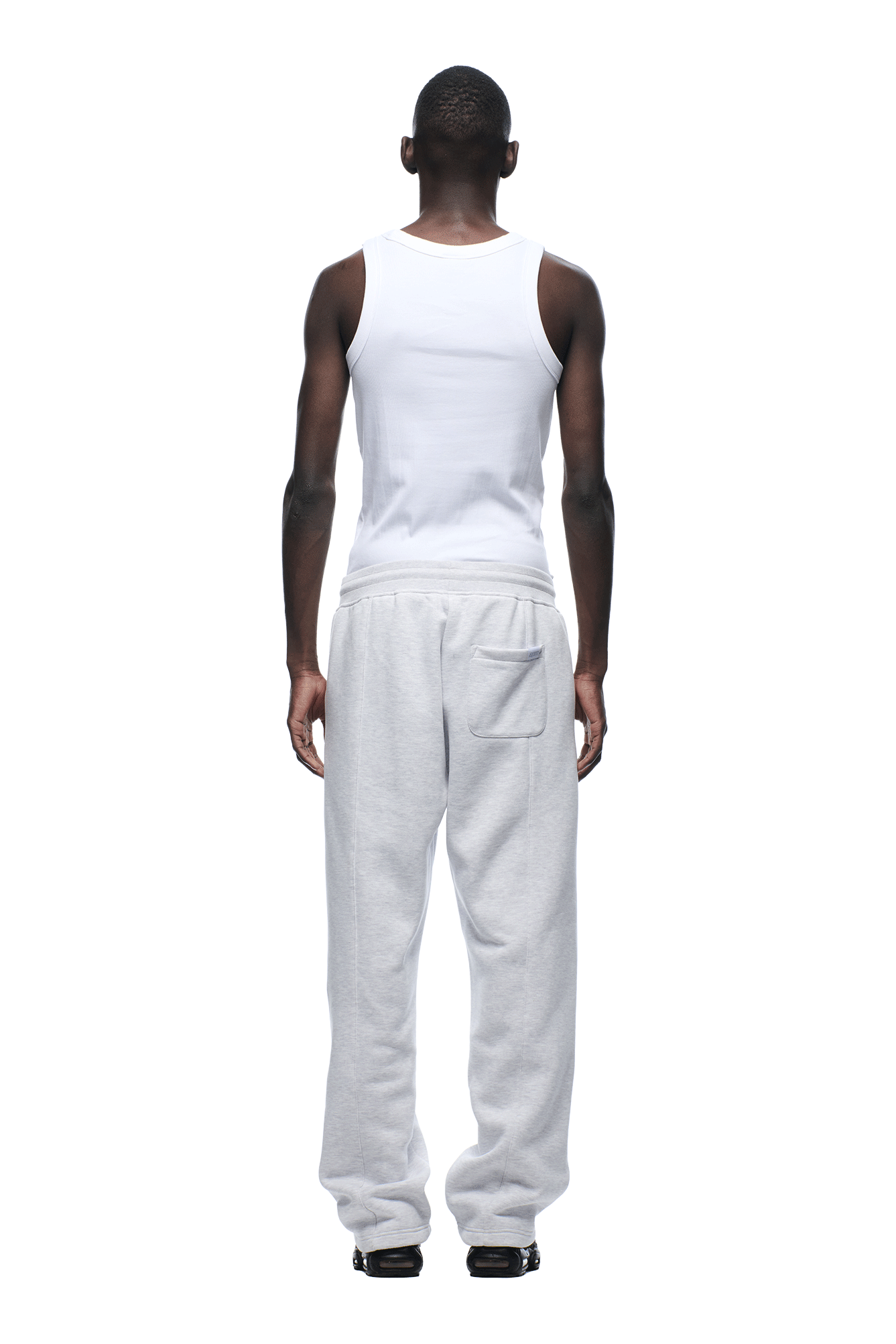 A man faces away against a plain white background, wearing a sleeveless white tank top, black shoes, and 6PM 6PM+ SLIM FIT JOGGER LIGHT GREY sweatpants.