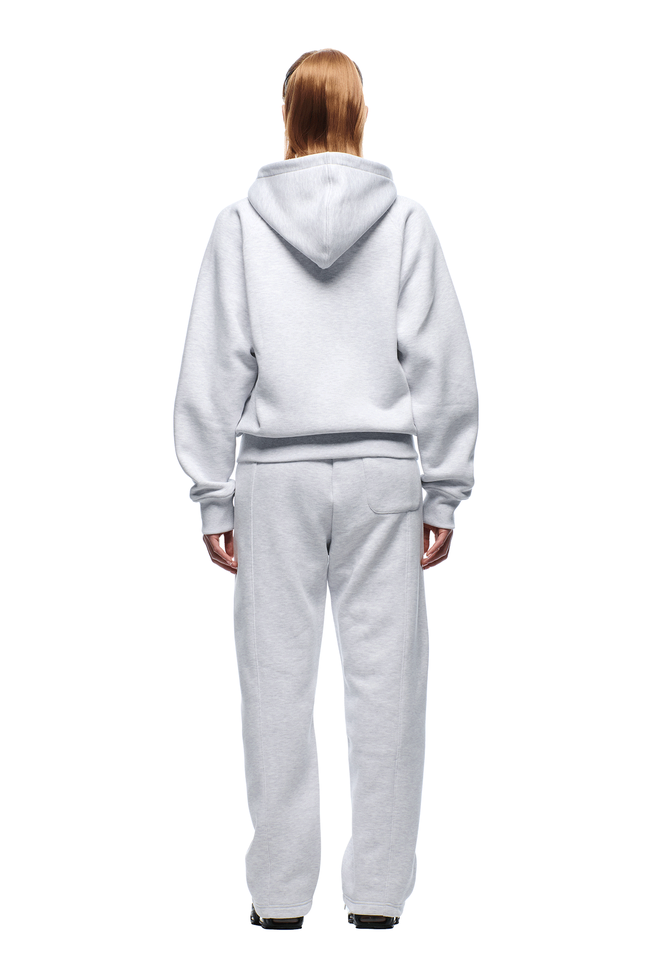 A person faces away from the camera wearing the 6PM 6PM+ SLIM ZIP HOODIE LIGHT GREY with the hood up, paired with matching sweatpants, their hands relaxed by their sides for a sleek look.