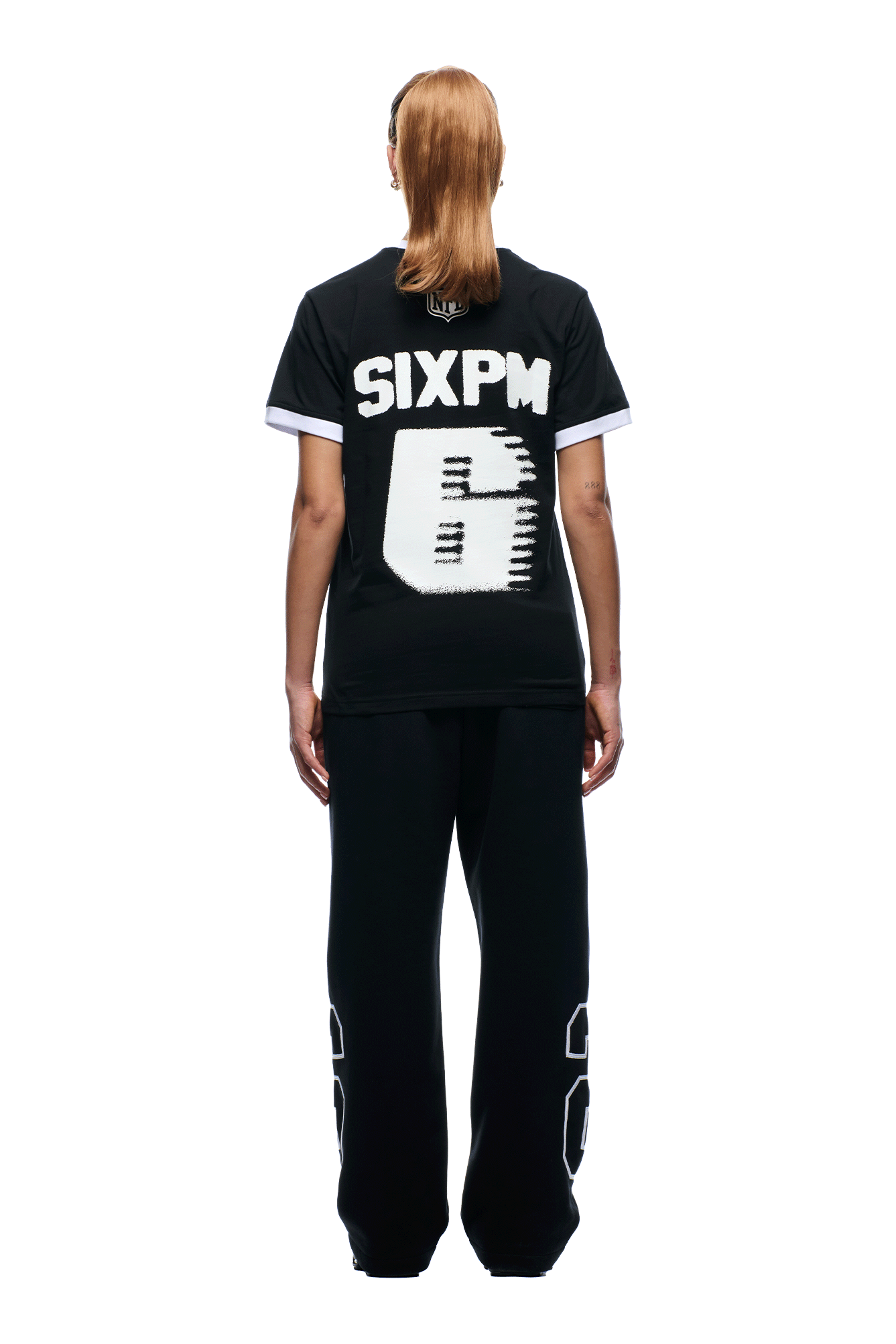 A person faces away, wearing the 6PM NFL BLURRED T-SHIRT in black with a pixelated white number 6 on the back, paired with black pants featuring outlined numbers near the ankles, against a plain white background.