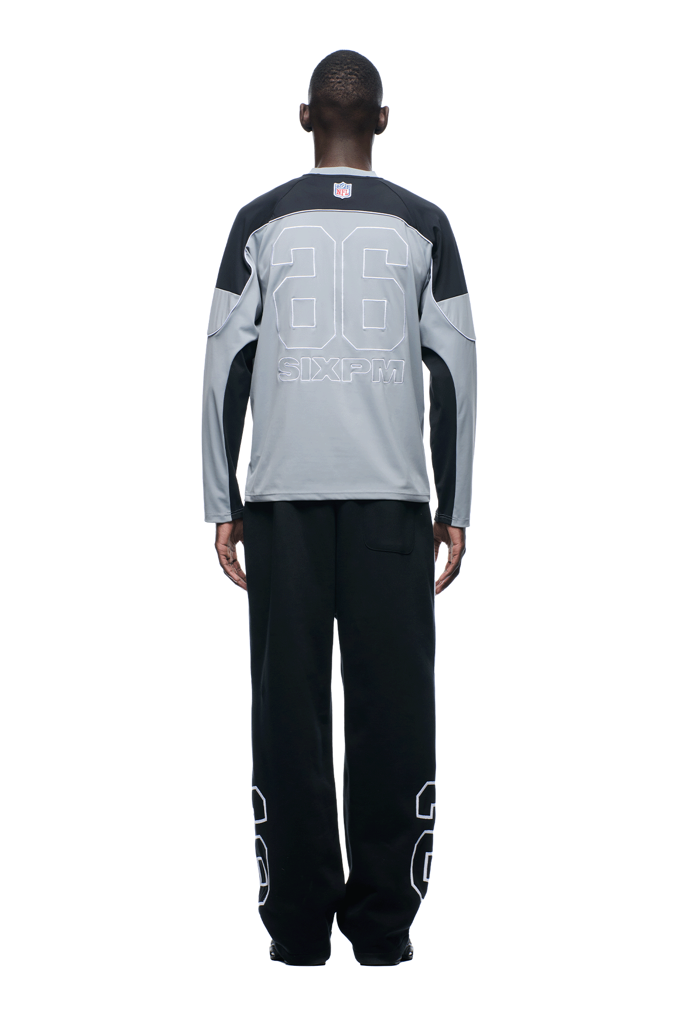 A person faces away, wearing the 6PM NFL SCUBA LONGSLEEVE GREY jersey with "86" and "6PM" on the back, paired with black pants that have a large "86" on the lower legs.