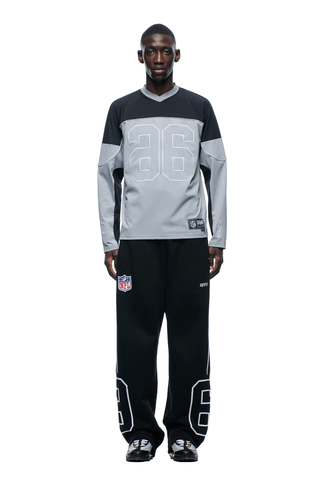 A person stands facing forward in a 6PM NFL SCUBA LONGSLEEVE GREY jersey with the number 26, paired with black pants featuring the NFL logo and number 26 by the knees. The background is plain white.