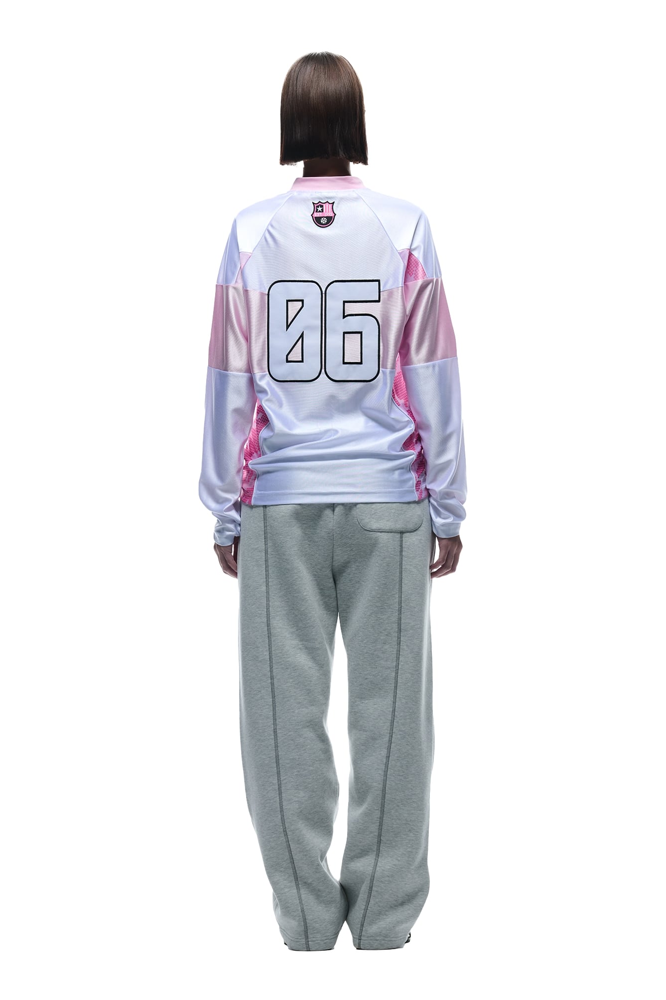 A person faces away, wearing the 6PM LONGSLEEVE JERSEY WHITE/PINK with 06 on the back and gray sweatpants against a plain white background.