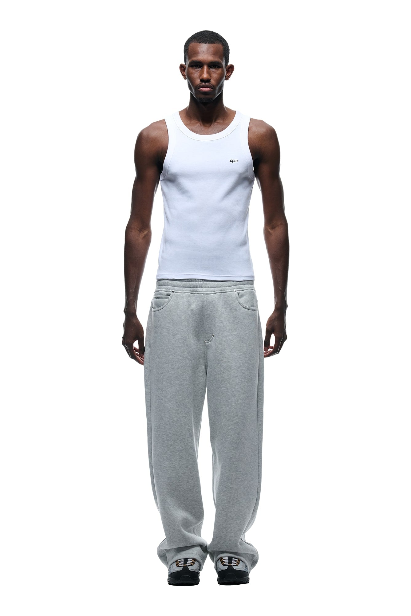 A man faces forward against a white background, wearing the 6PM X-TRA WIDE 5-POCKET JOGGER GREY, a white sleeveless tank top, and dark sneakers.