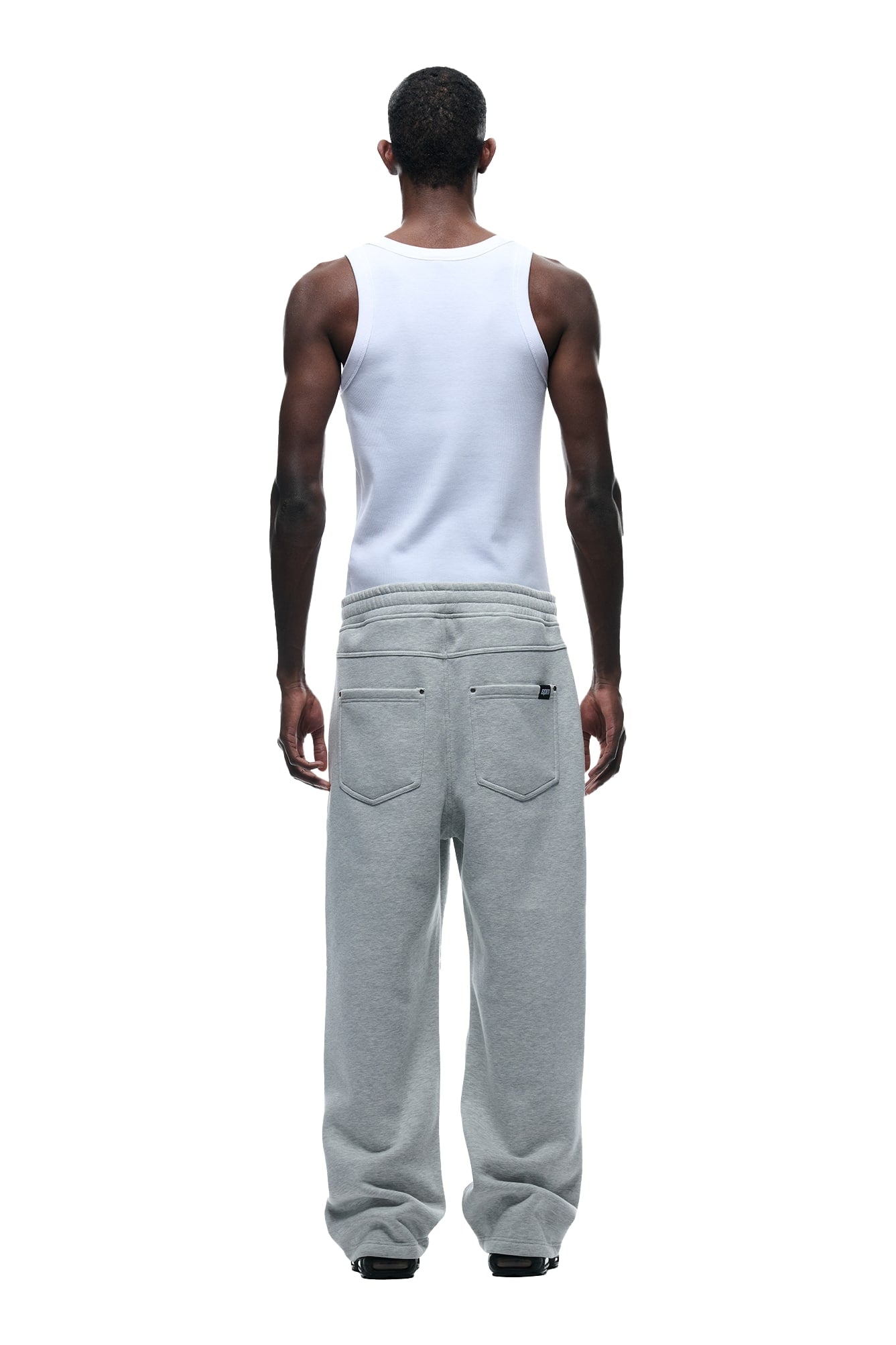 A person stands with their back to the camera wearing 6PM’s X-TRA WIDE 5-POCKET JOGGER GREY and a white tank top against a plain white background.