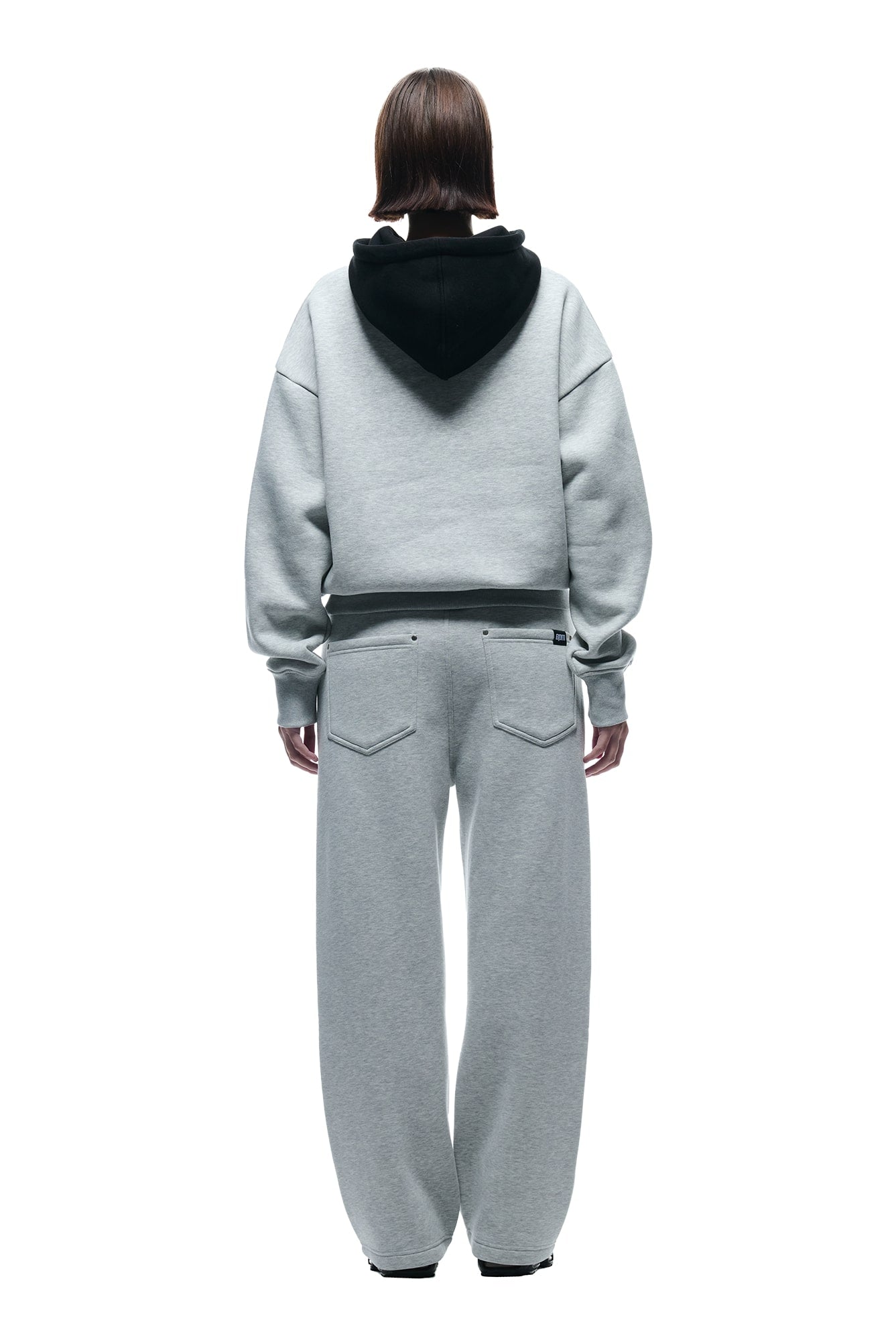 A person with straight brown hair faces away, wearing the 6PM CREWNECK HOODIE GREY/BLACK and matching gray sweatpants against a white background.