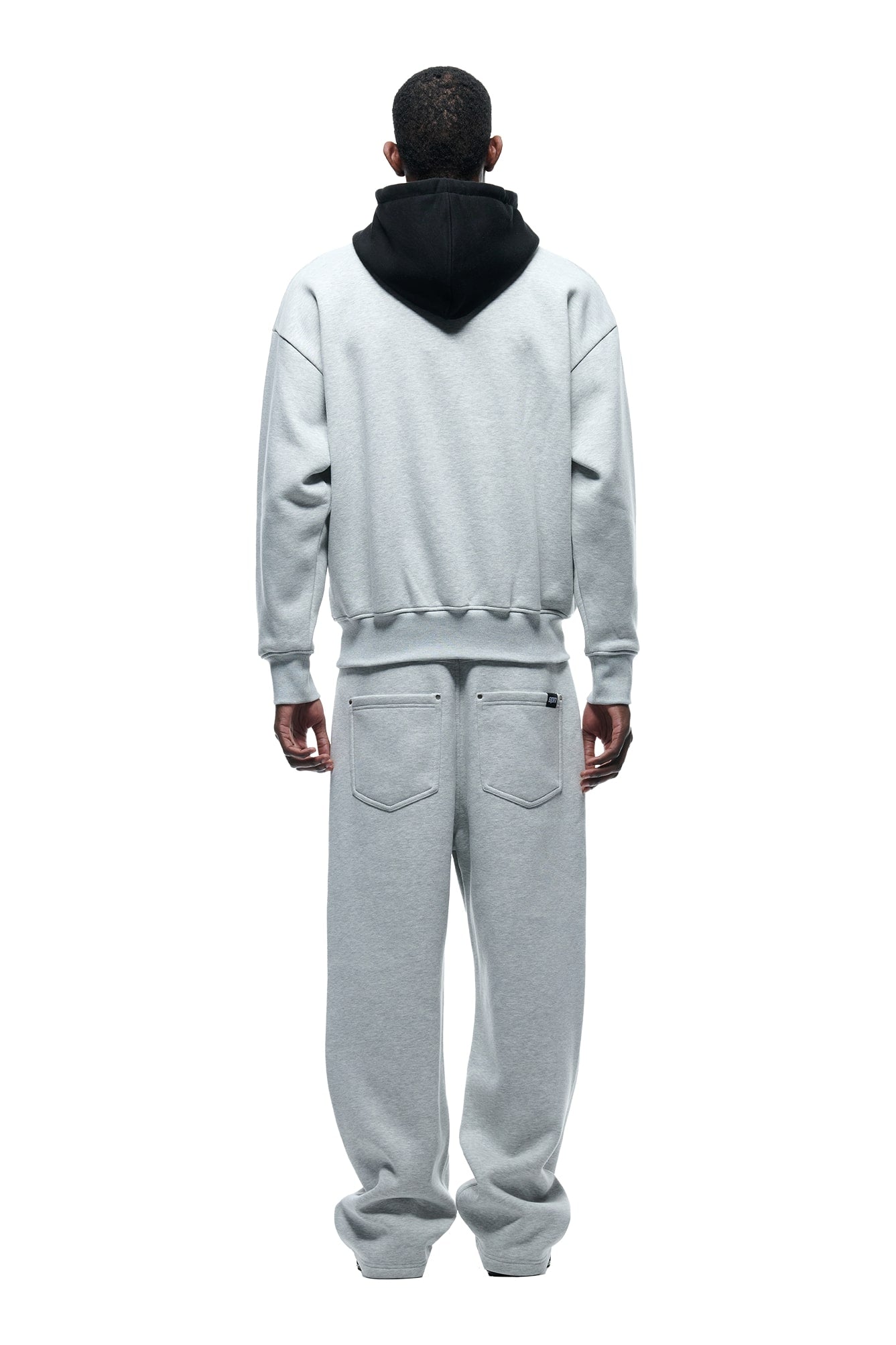 A person faces away, wearing the 6PM CREWNECK HOODIE GREY/BLACK and matching light gray sweatpants. The loose-fit, casual outfit stands out against a plain white background.
