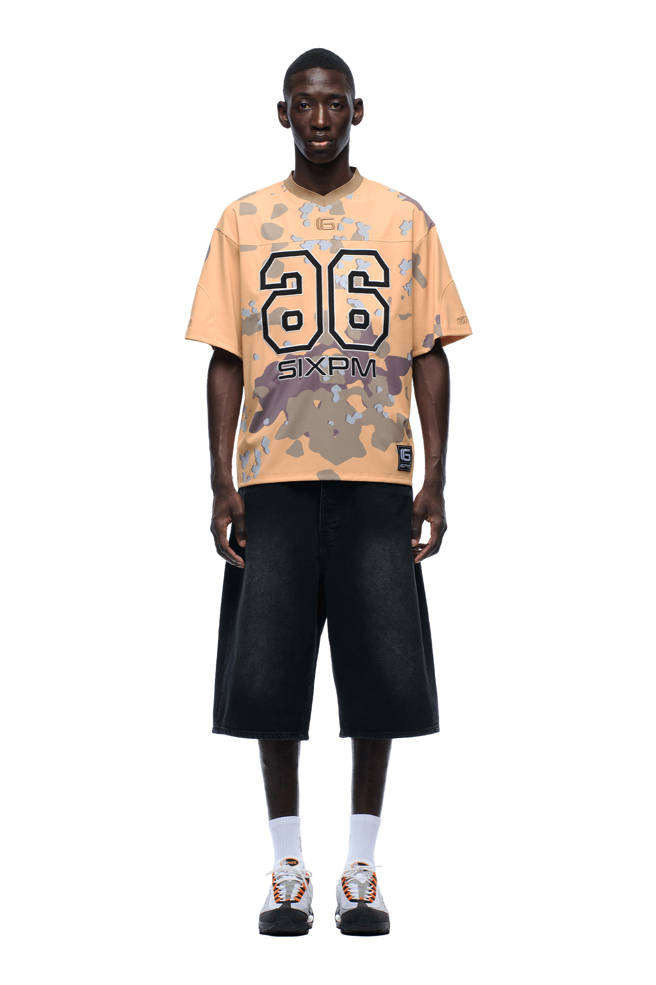 A man faces forward wearing the CAMO JERSEY BURRO by 6PM with number 26, black wide knee-length shorts, white socks, and sneakers. The background is transparent.