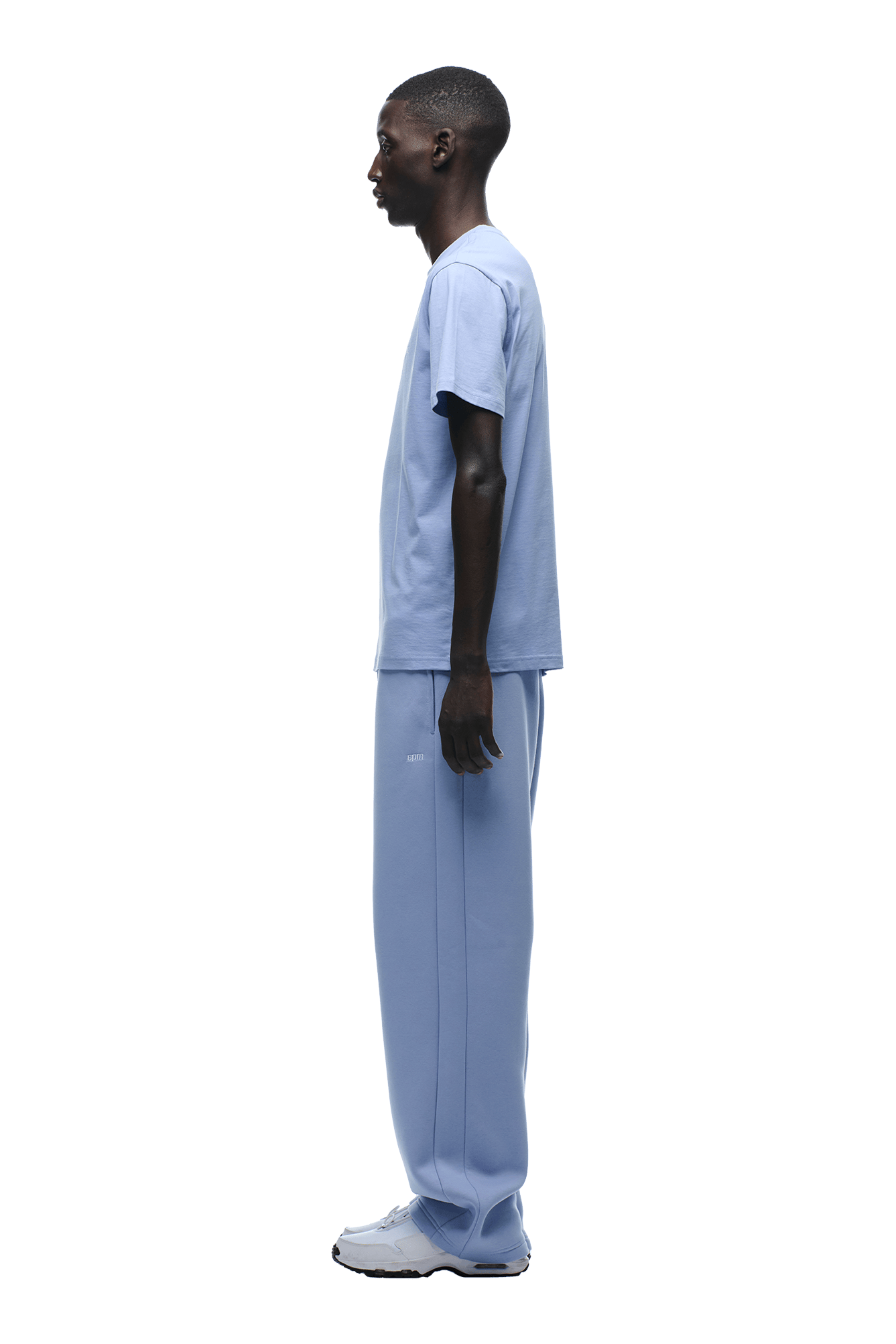 A man in profile faces left, rocking effortless style in the 6PM T-SHIRT REGULAR FIT SOFT VIOLET, matching sweatpants, and white sneakers against a plain background—proving less is more.
