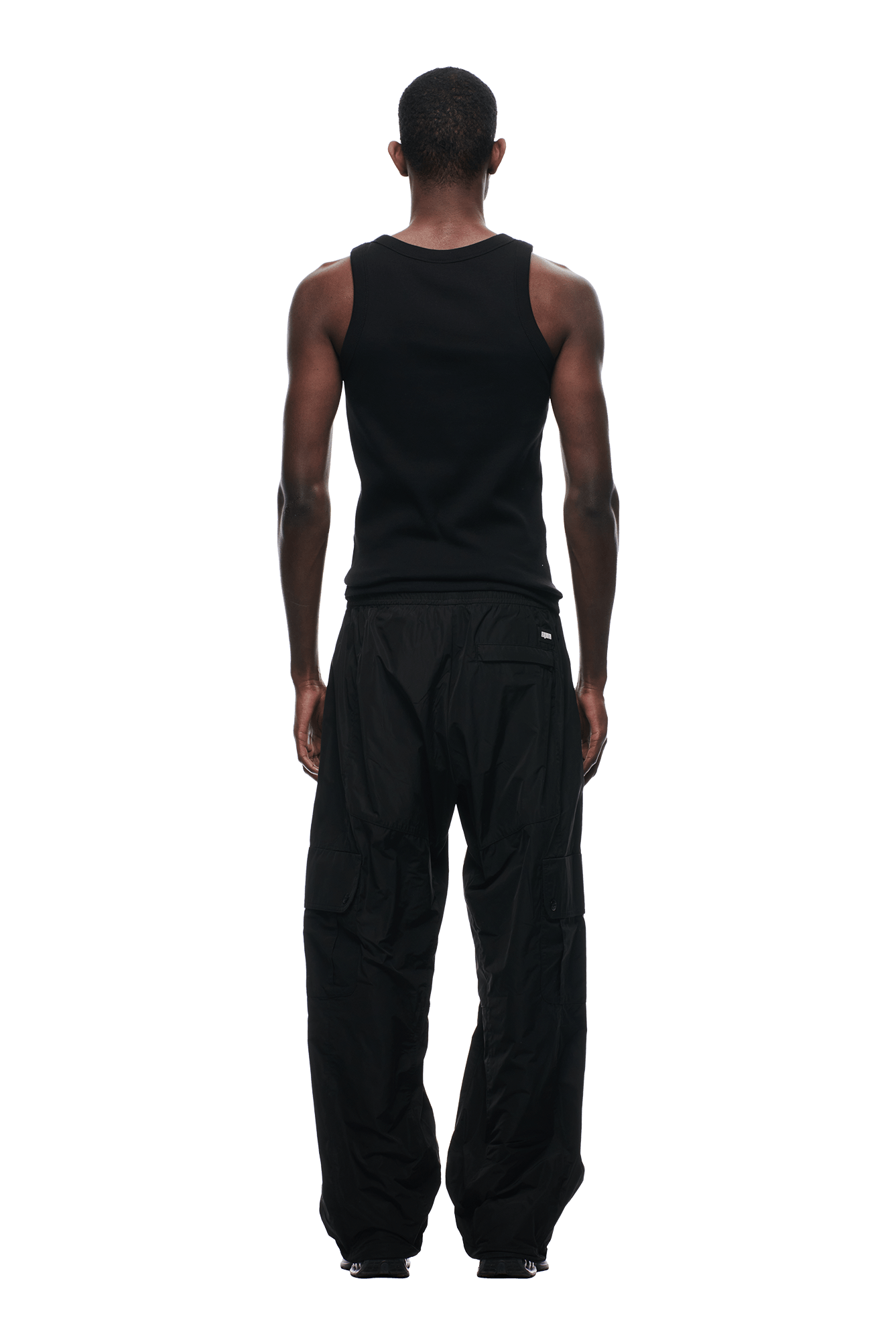 A man faces away against a transparent background, wearing 6PM NYLON CARGO PANTS BLACK and a sleeveless black tank top, with his arms relaxed at his sides.