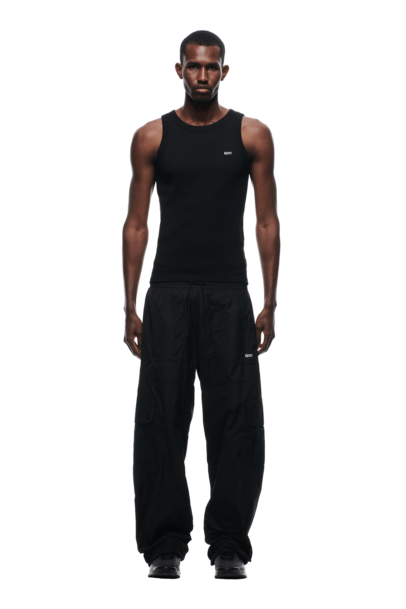 A man faces forward in a fitted black tank top, 6PM NYLON CARGO PANTS BLACK, and black shoes. Background is transparent.