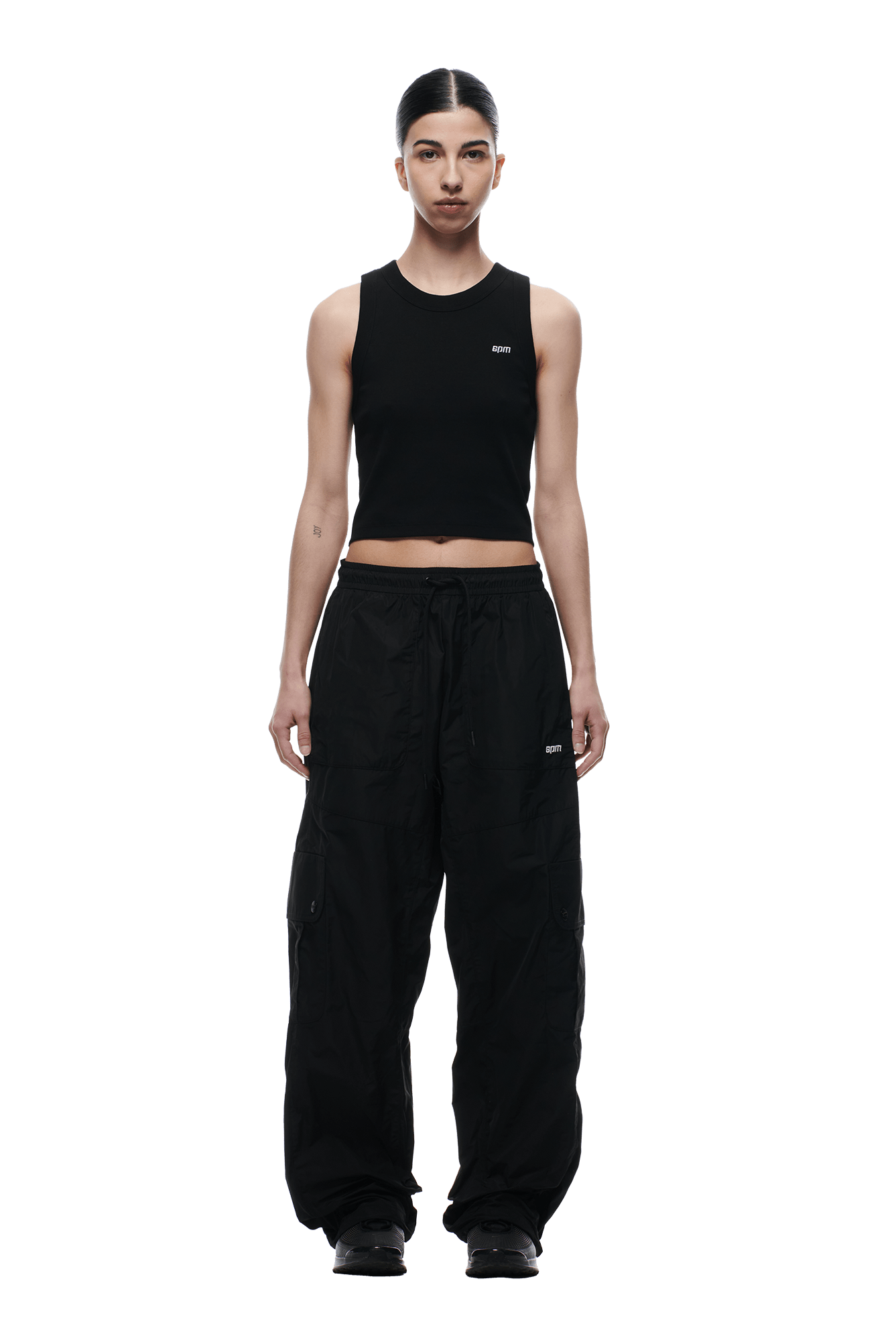 A person stands facing forward, wearing a black sleeveless crop top and 6PM NYLON CARGO PANTS BLACK with black shoes. Their hair is center-parted and tied back. The background is transparent.
