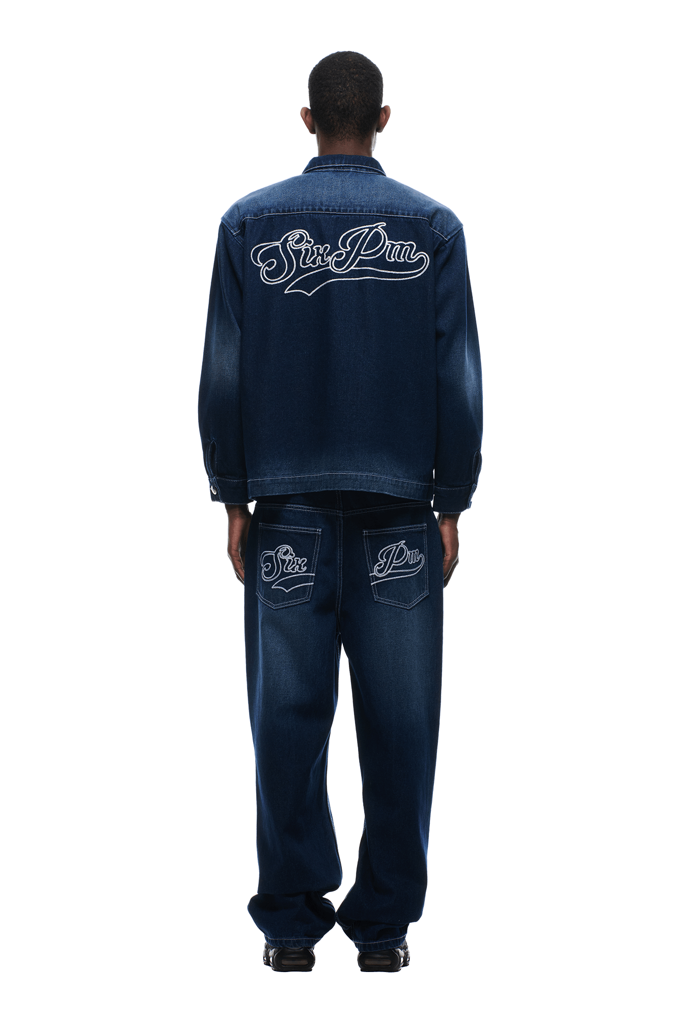 A person stands facing away, wearing the 6PM SCRIPT LOGO DENIM JACKET DARK BLUE with matching baggy jeans featuring white "Sin Périn" embroidery on the jacket back and jeans pockets. The background is plain white.