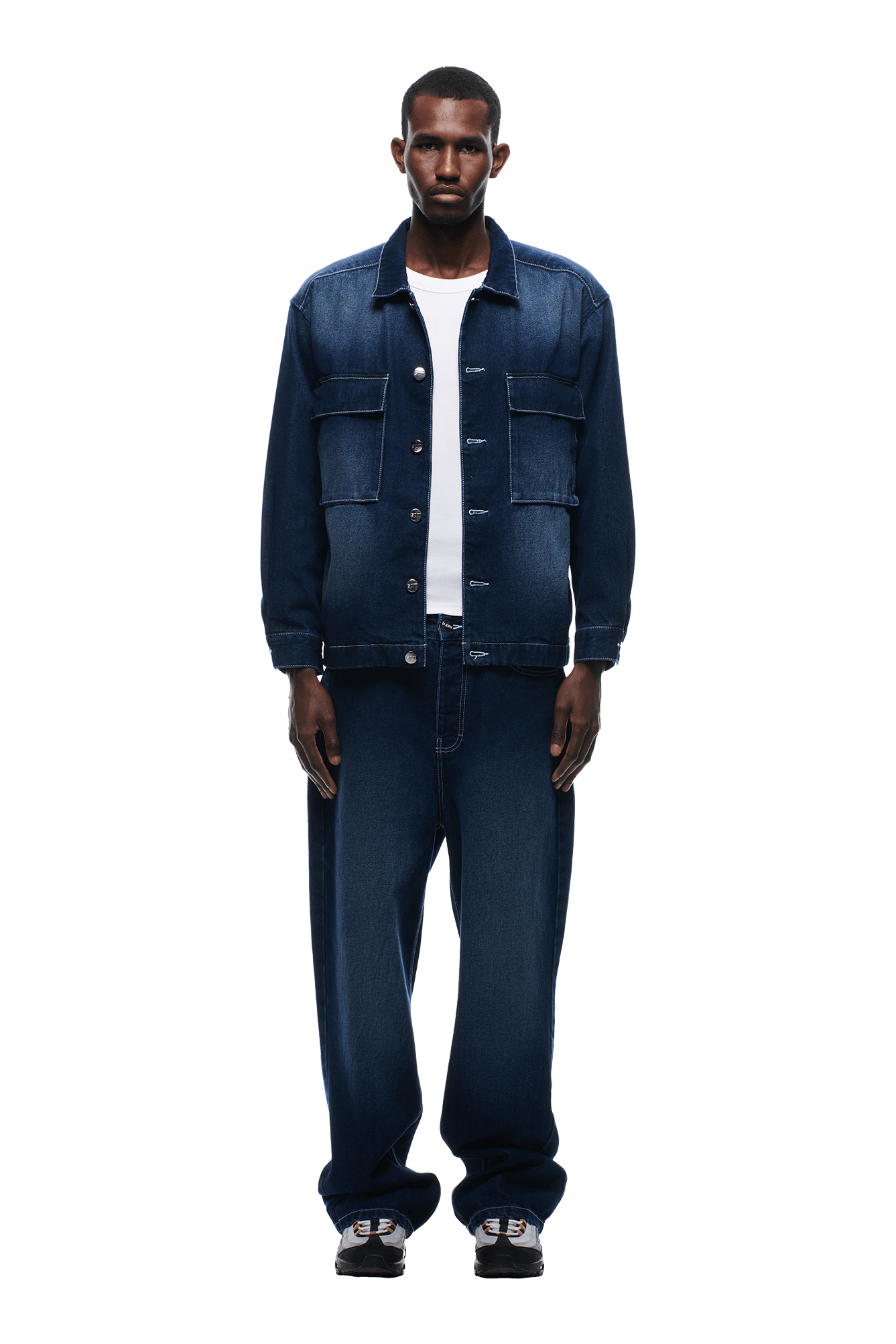 A man faces forward wearing the 6PM SCRIPT LOGO DENIM JACKET DARK BLUE with matching wide-leg jeans, a white t-shirt, and black sneakers, set against a plain white background.