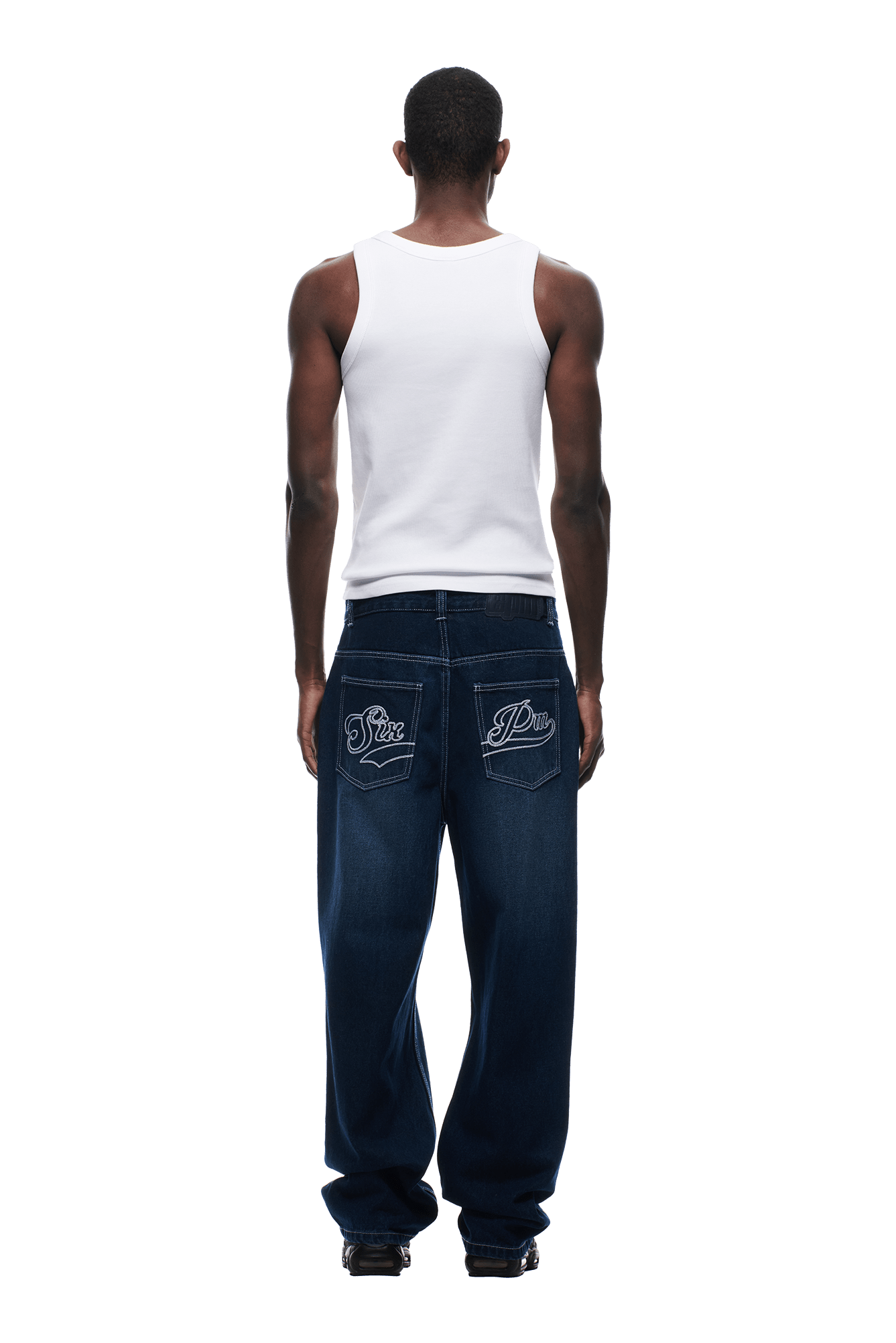 A man faces away, wearing a white tank top and 6PM SCRIPT LOGO DENIM WASHED DARK BLUE jeans featuring embroidered back pocket designs, set against a plain white background.