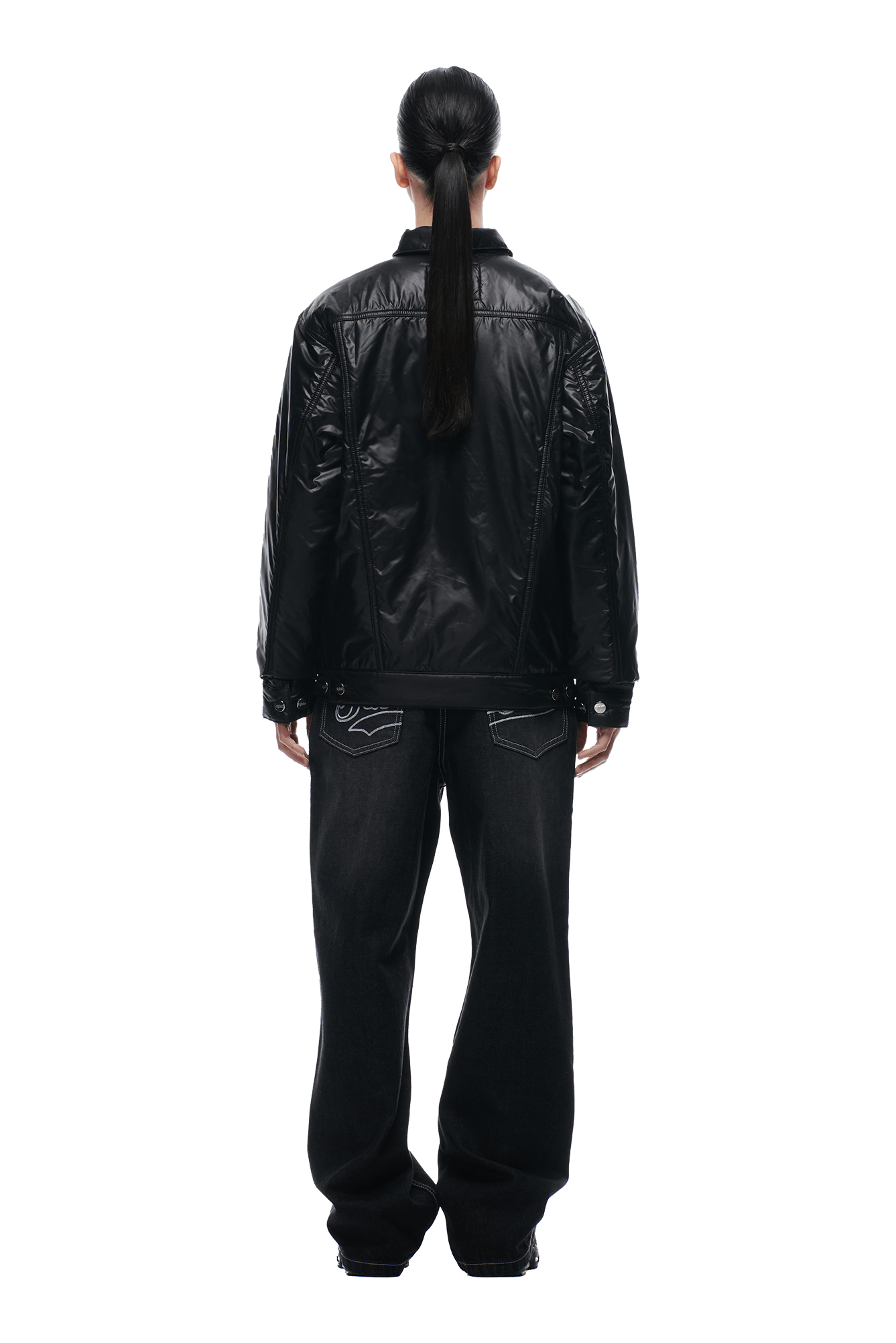 A person with long, dark hair in a low ponytail stands with their back to the camera, wearing the 6PM PADDED TRUCKER JACKET BLACK and loose black jeans against a plain white background.