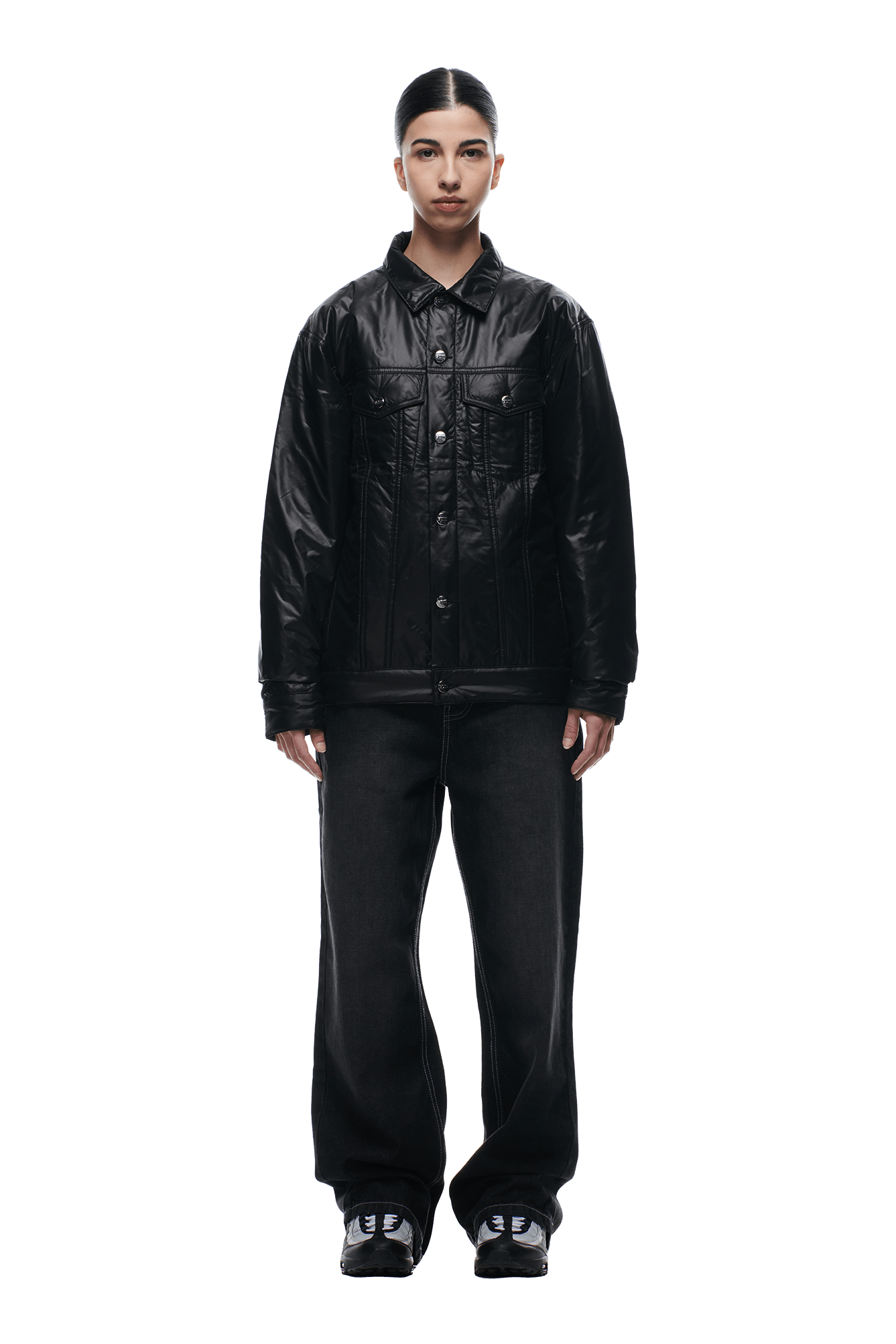 A person stands facing forward, wearing the 6PM PADDED TRUCKER JACKET BLACK with loose black pants and black sneakers. Their dark hair is neatly styled back against a plain white background.