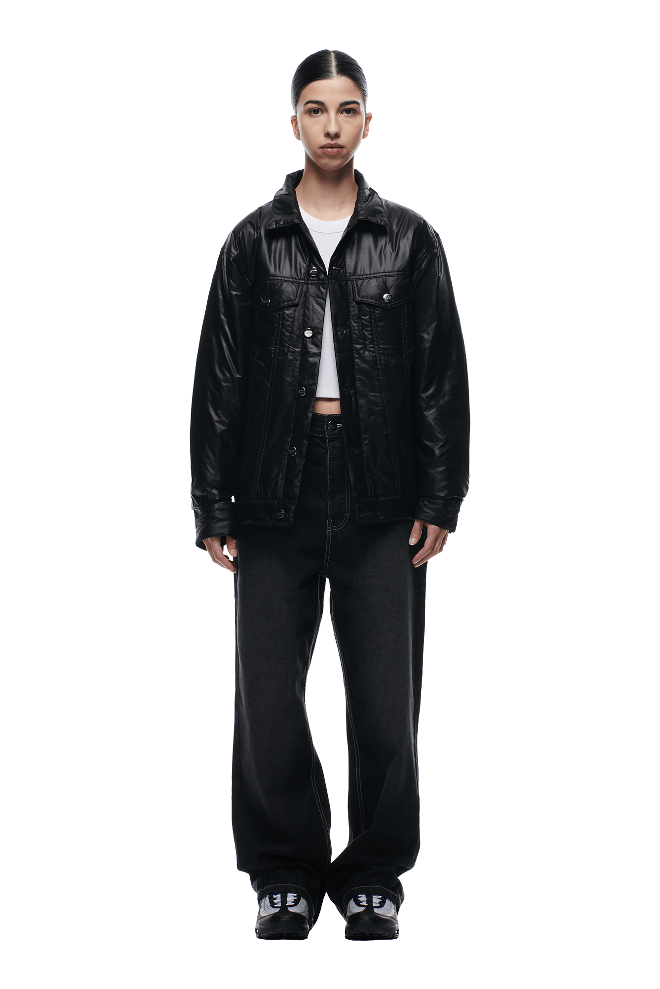 A person stands facing forward, wearing the 6PM PADDED TRUCKER JACKET BLACK over a white crop top, with loose black jeans and black sneakers. Their hair is parted in the middle and tied back, set against a plain white background.