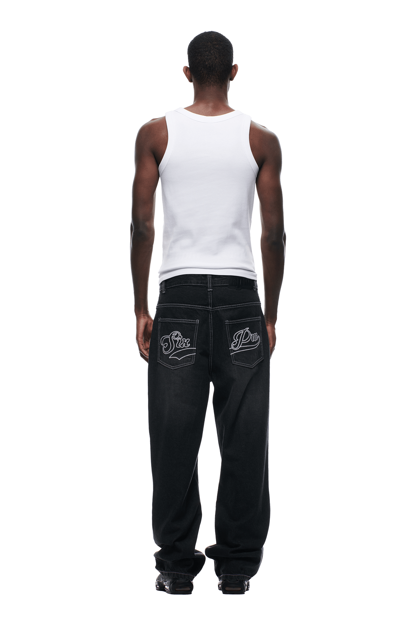 A person faces away, wearing a white tank top and 6PM SCRIPT LOGO DENIM WASHED BLACK jeans featuring white embroidery on the back pockets, set against a plain white background.