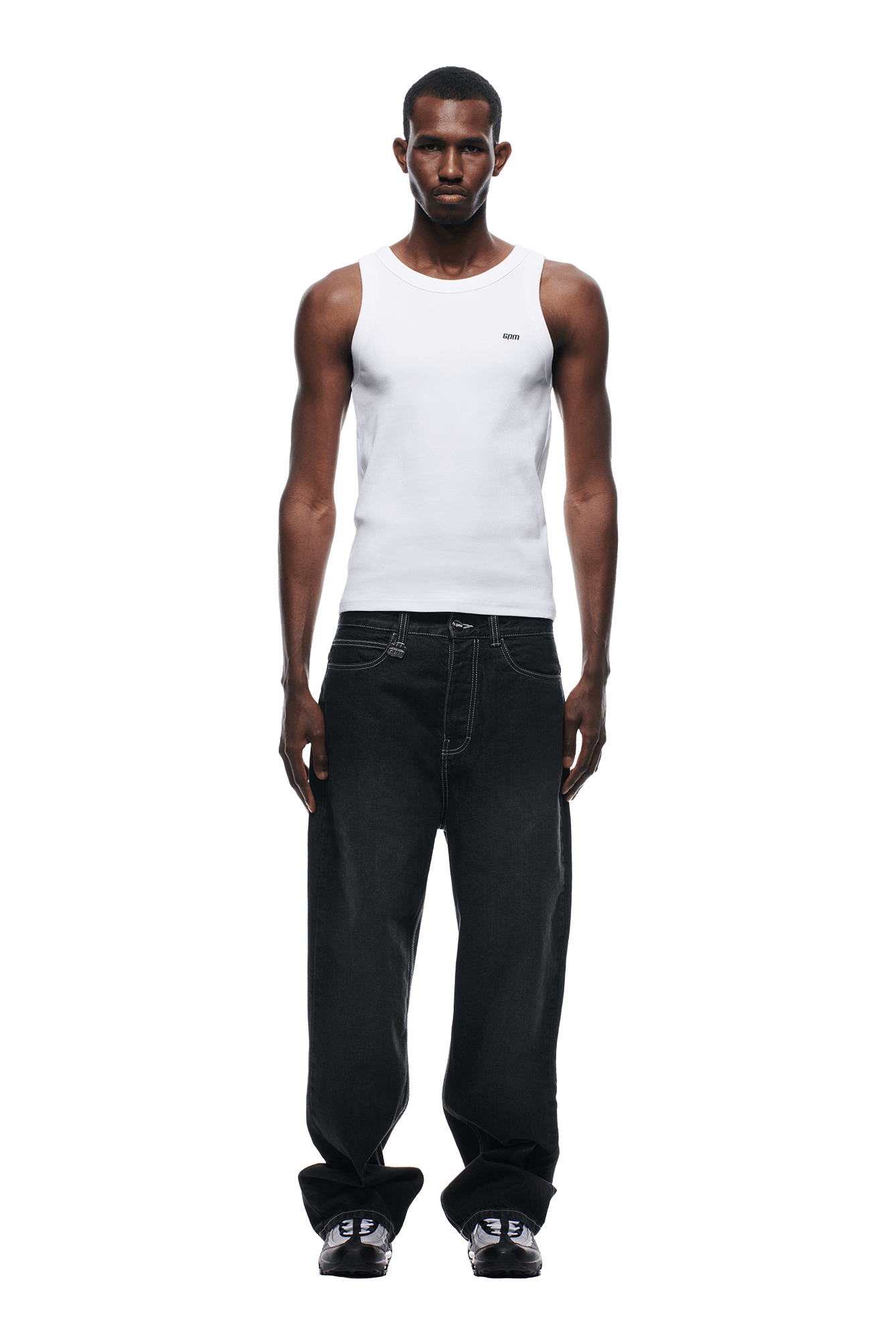 A man faces forward against a plain white background, wearing a fitted white tank top, 6PM SCRIPT LOGO DENIM WASHED BLACK jeans with white stitching, and black sneakers.