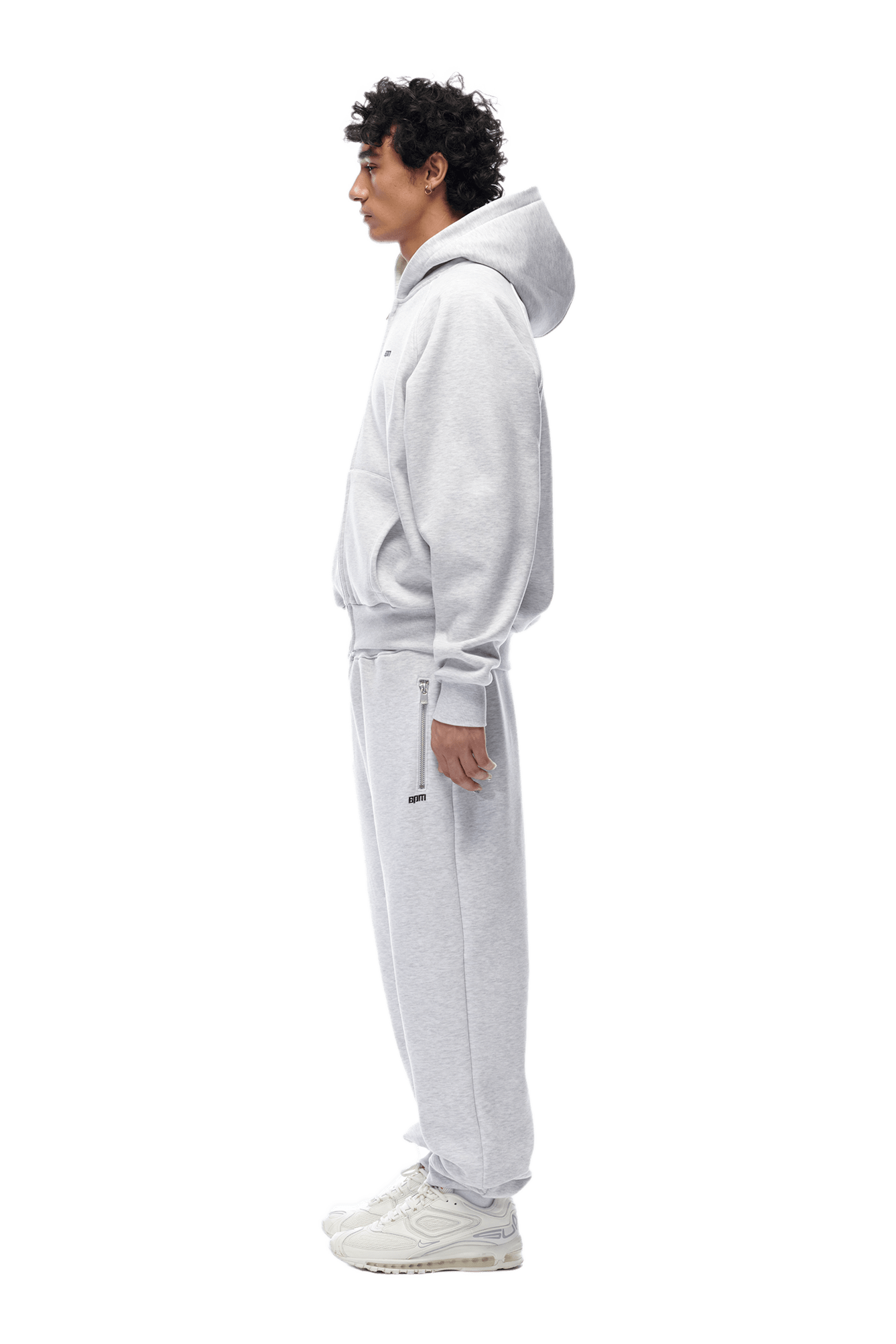 A person in profile wears the 6PM ZIP HOODIE LIGHT GREY with matching sweatpants and white sneakers, styled for a clean everyday look, against a transparent background.