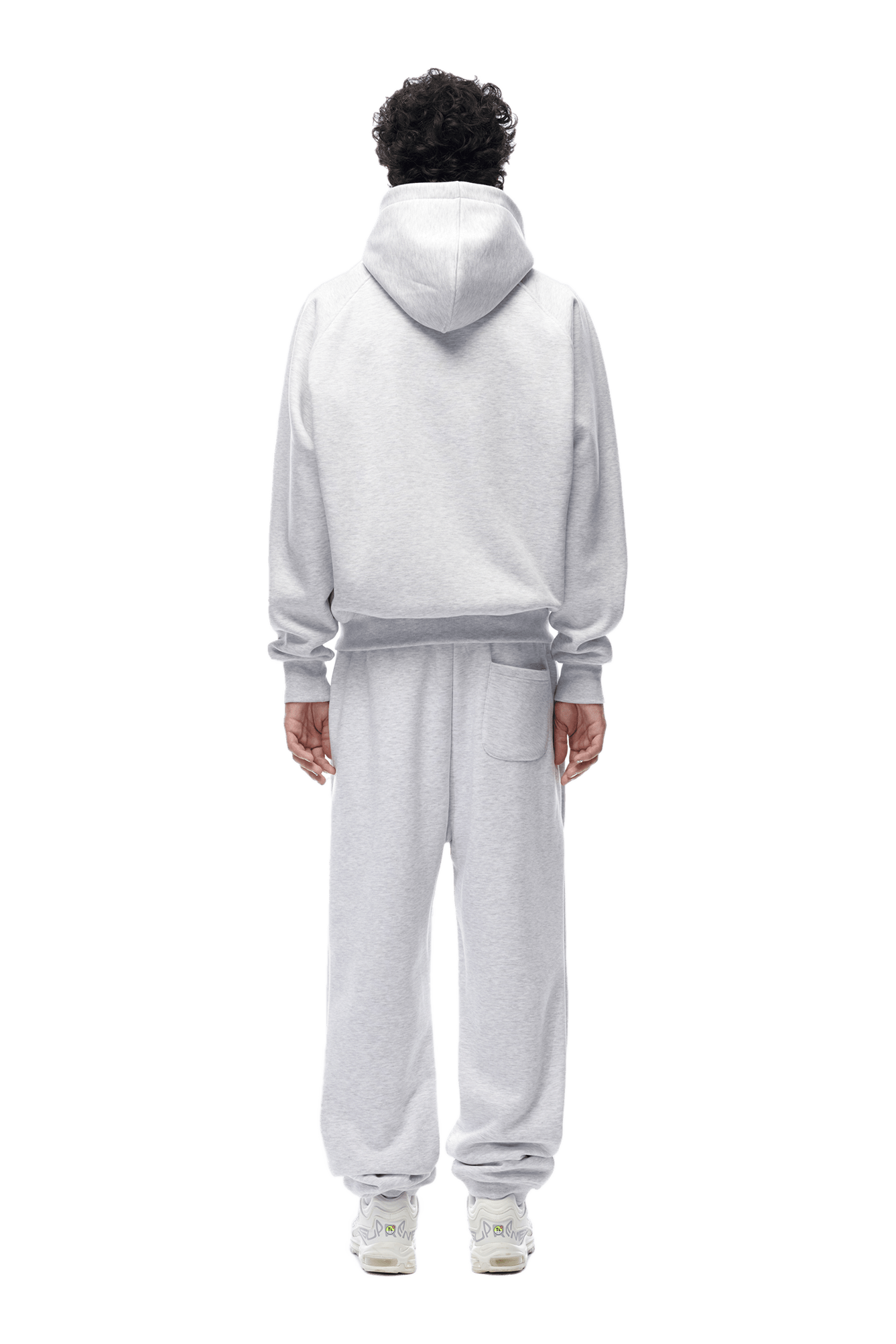 A person stands facing away against a plain white background, wearing the 6PM ZIP HOODIE LIGHT GREY with matching sweatpants and white sneakers.