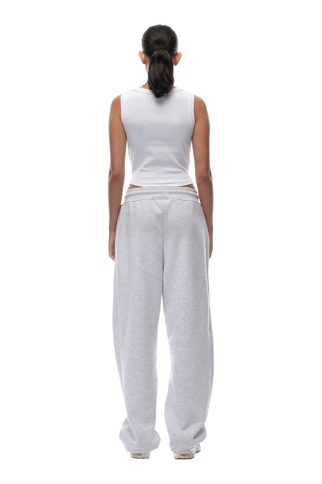 A woman with dark hair in a ponytail stands with her back to the camera, wearing a white sleeveless top and OPEN LEG JOGGER LIGHT GREY pants.