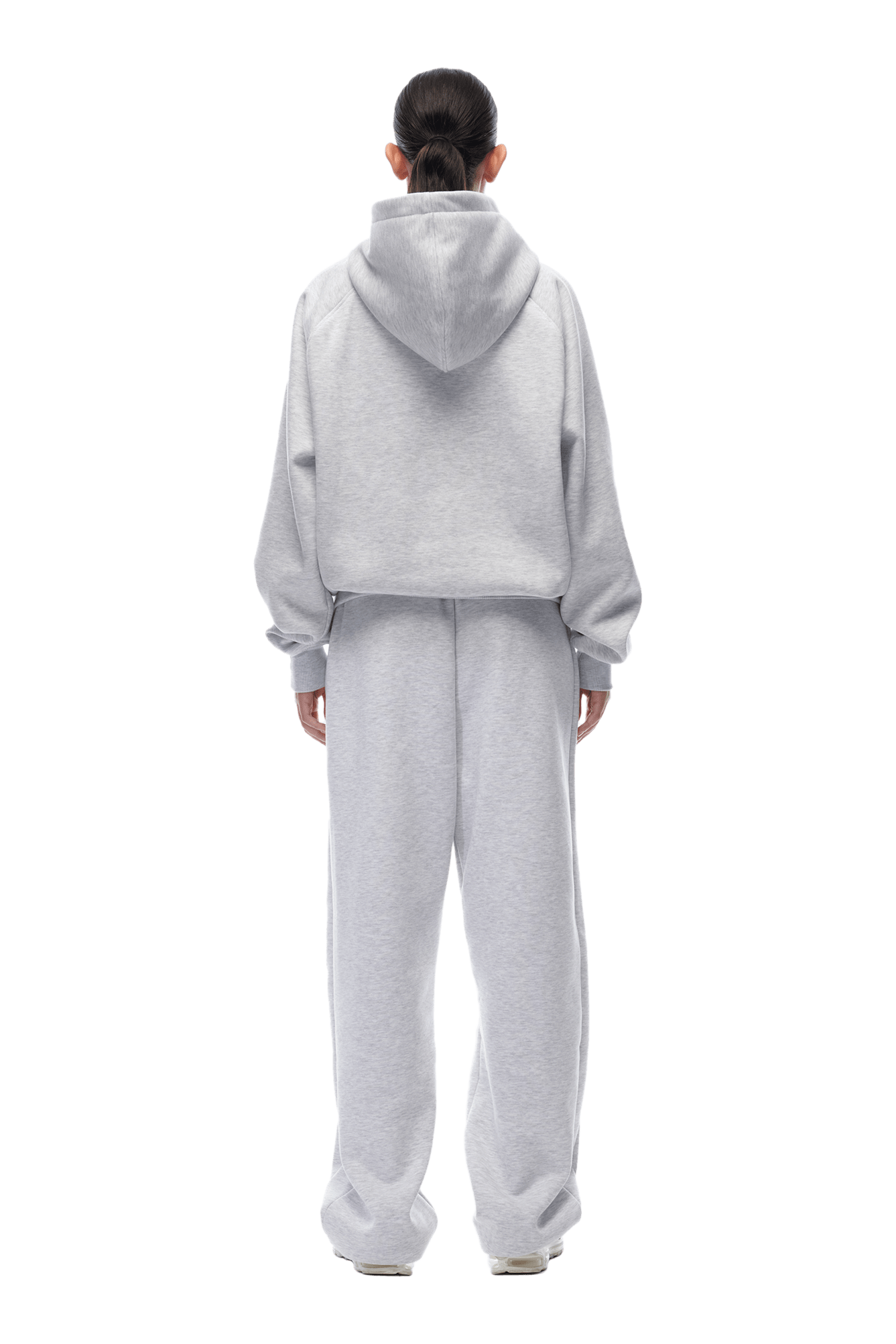 A person with tied-back hair faces away, wearing the 6PM HOODIE LIGHT GREY and matching sweatpants. The light gray raglan-sleeved hoodie has the hood down, ideal for daily wear, shown against a plain transparent background.