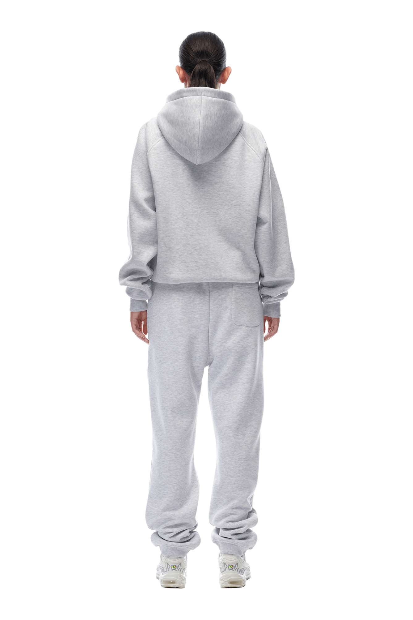 A person with dark hair tied back faces away, wearing the 6PM ZIP HOODIE LIGHT GREY and matching sweatpants with white sneakers. This clean, minimalist look is perfect for daily wear, set against a plain background.