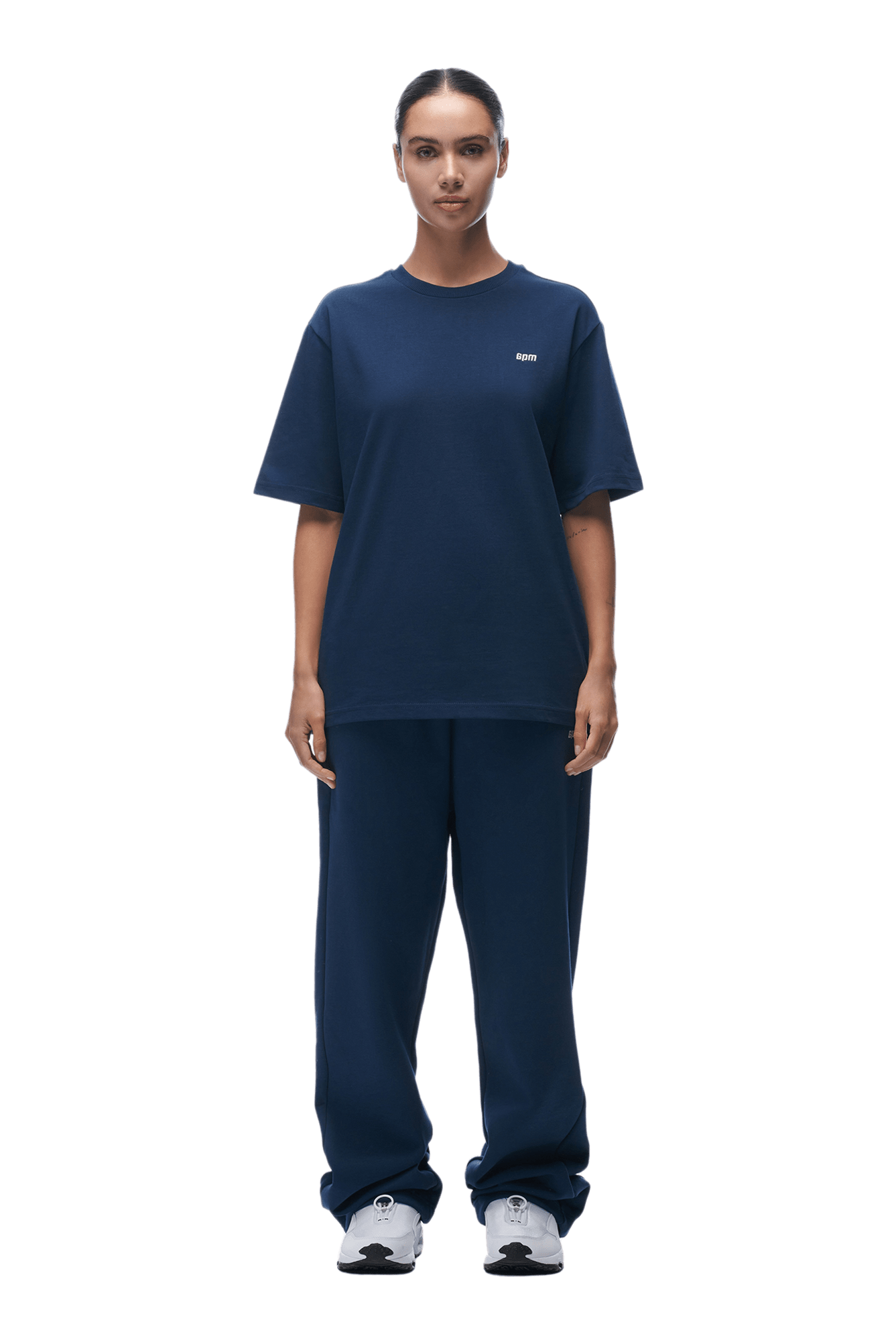 A person stands facing forward wearing a classic, loose-fitting 6PM T-SHIRT NAVY and matching sweatpants with white sneakers, on a transparent background.