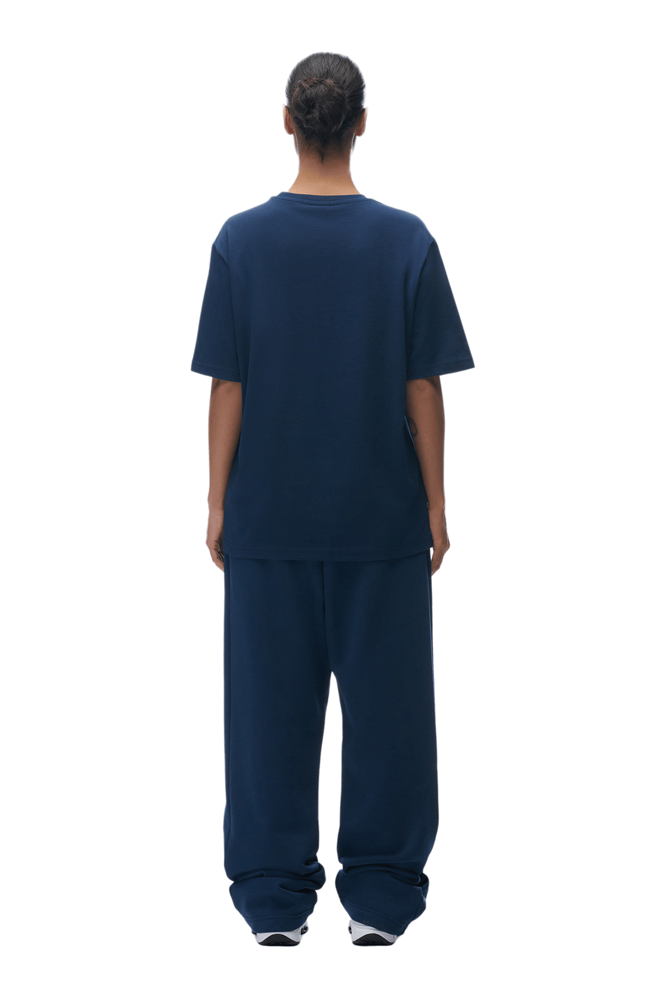 A person with hair tied back stands with their back to the camera, wearing the 6PM T-SHIRT NAVY and matching baggy pants, paired with white sneakers. The background is transparent.