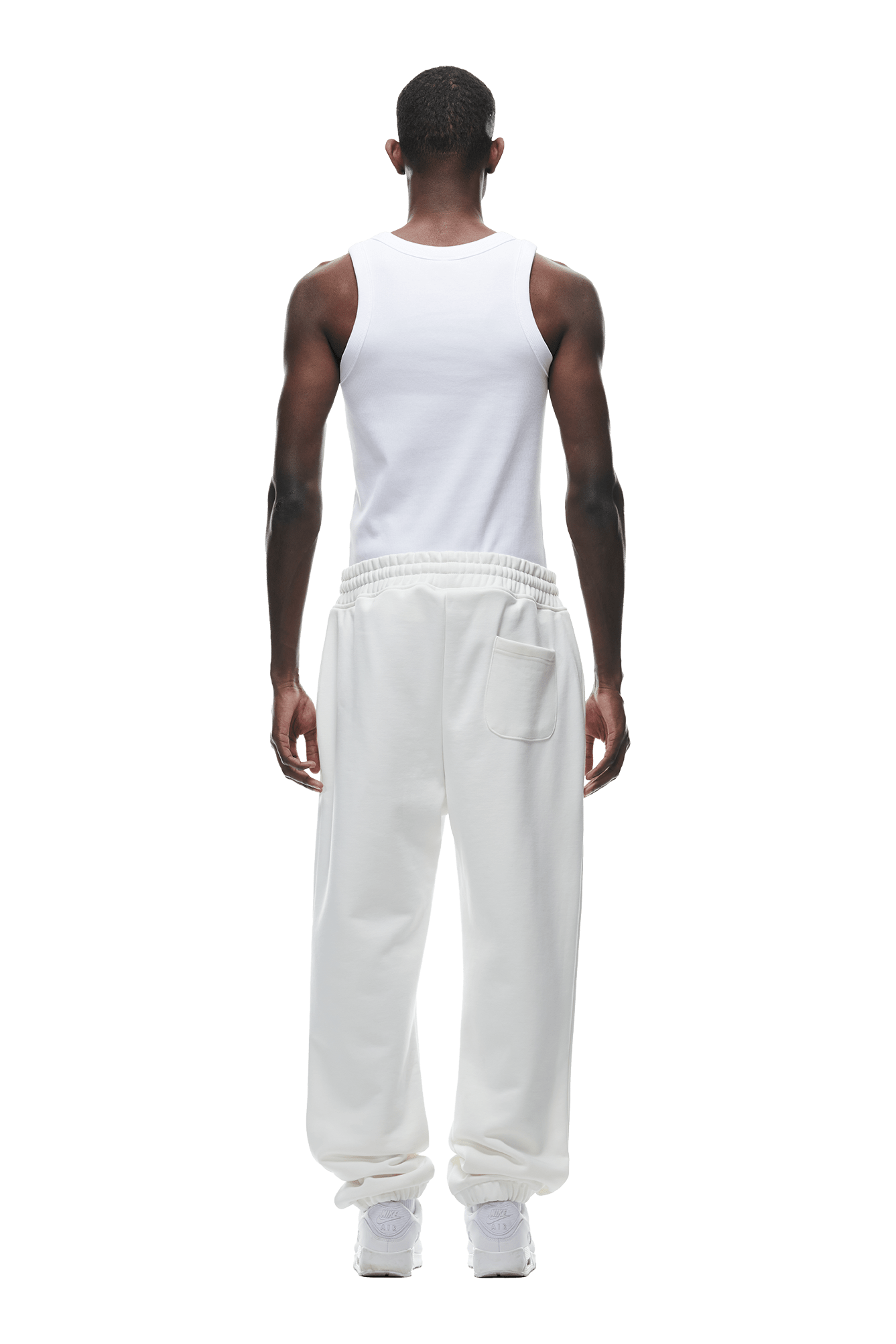 A man stands with his back to the camera, wearing 6PM’s CUFF JOGGER COCONUT WHITE—classic fit sweatpants featuring a back pocket and cuffed legs—paired with a white tank top and sneakers, set against a plain background.